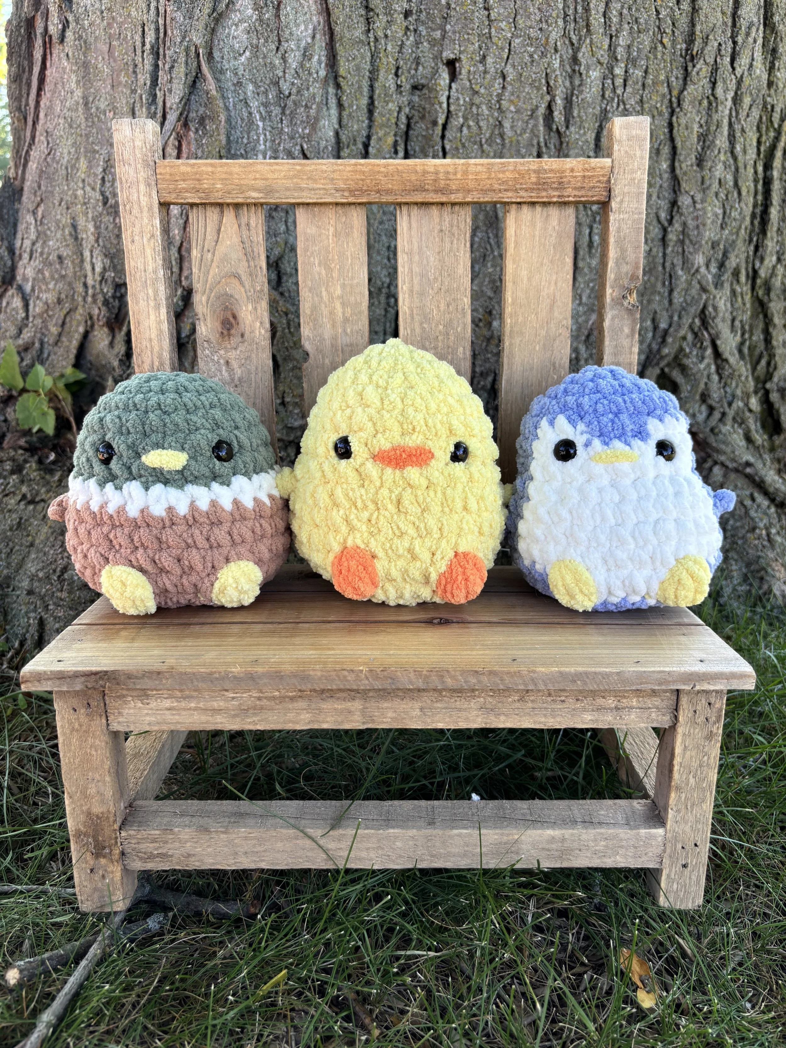 Three crochet round bird plushies, chick, mallard, and penguin, on wooden bench