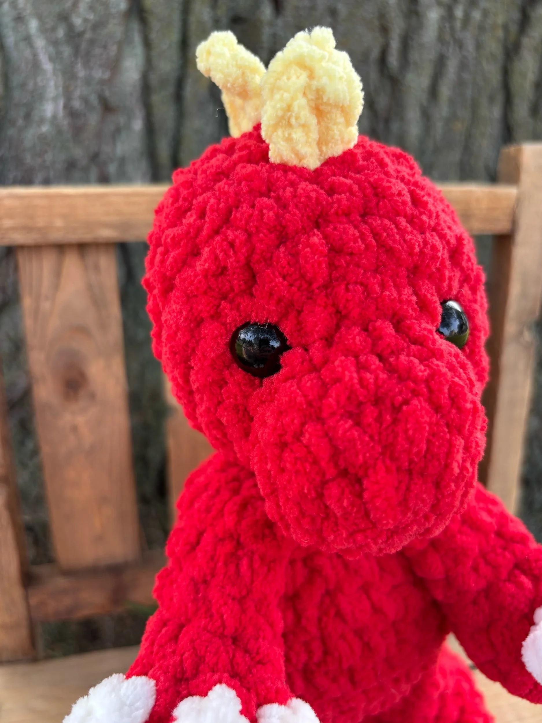 Close-up of handmade crochet T-Rex plushie face showing yellow crest and safety eyes