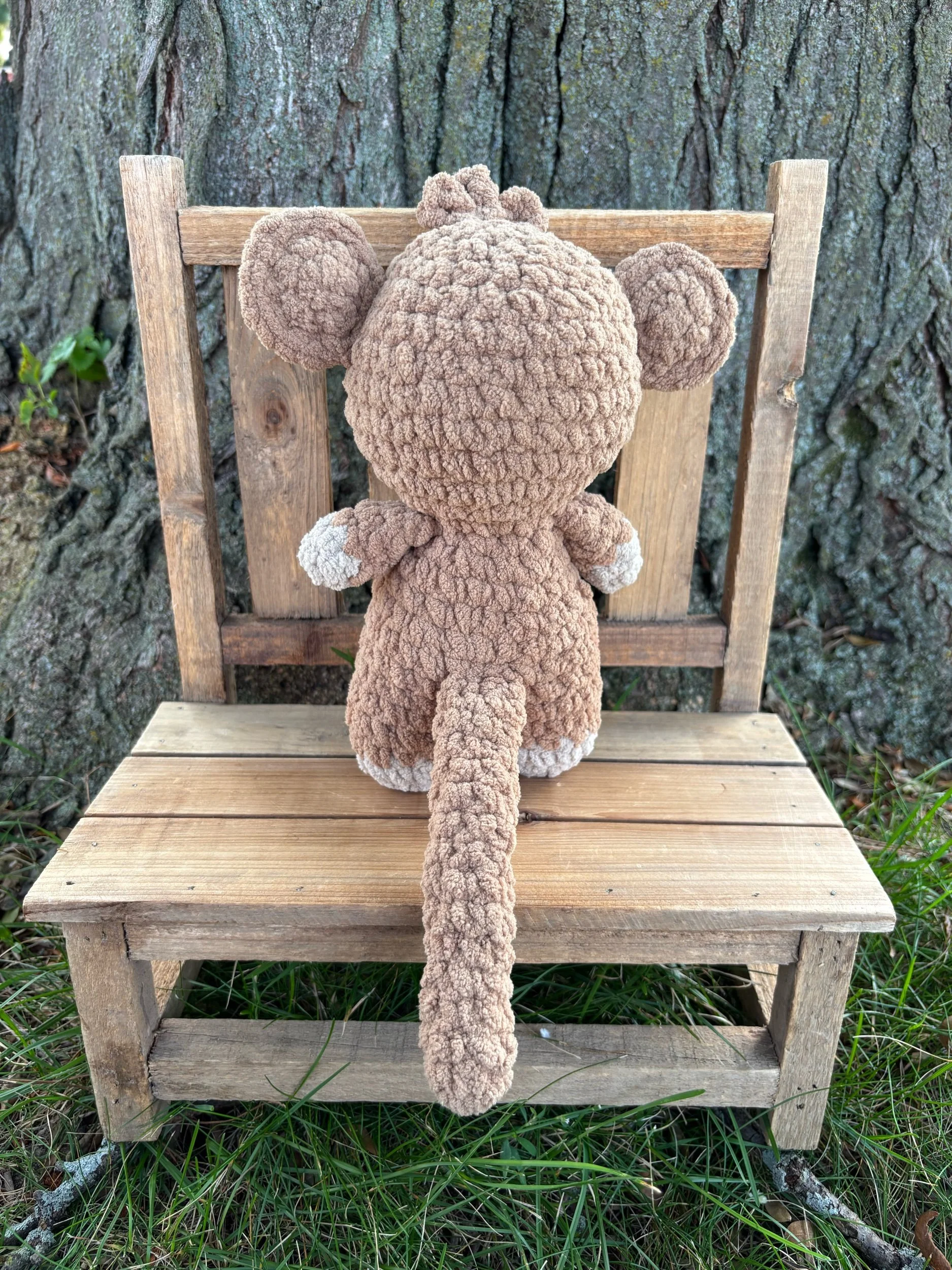 Back view of handmade crochet monkey plushie showing tail and cream paw pads