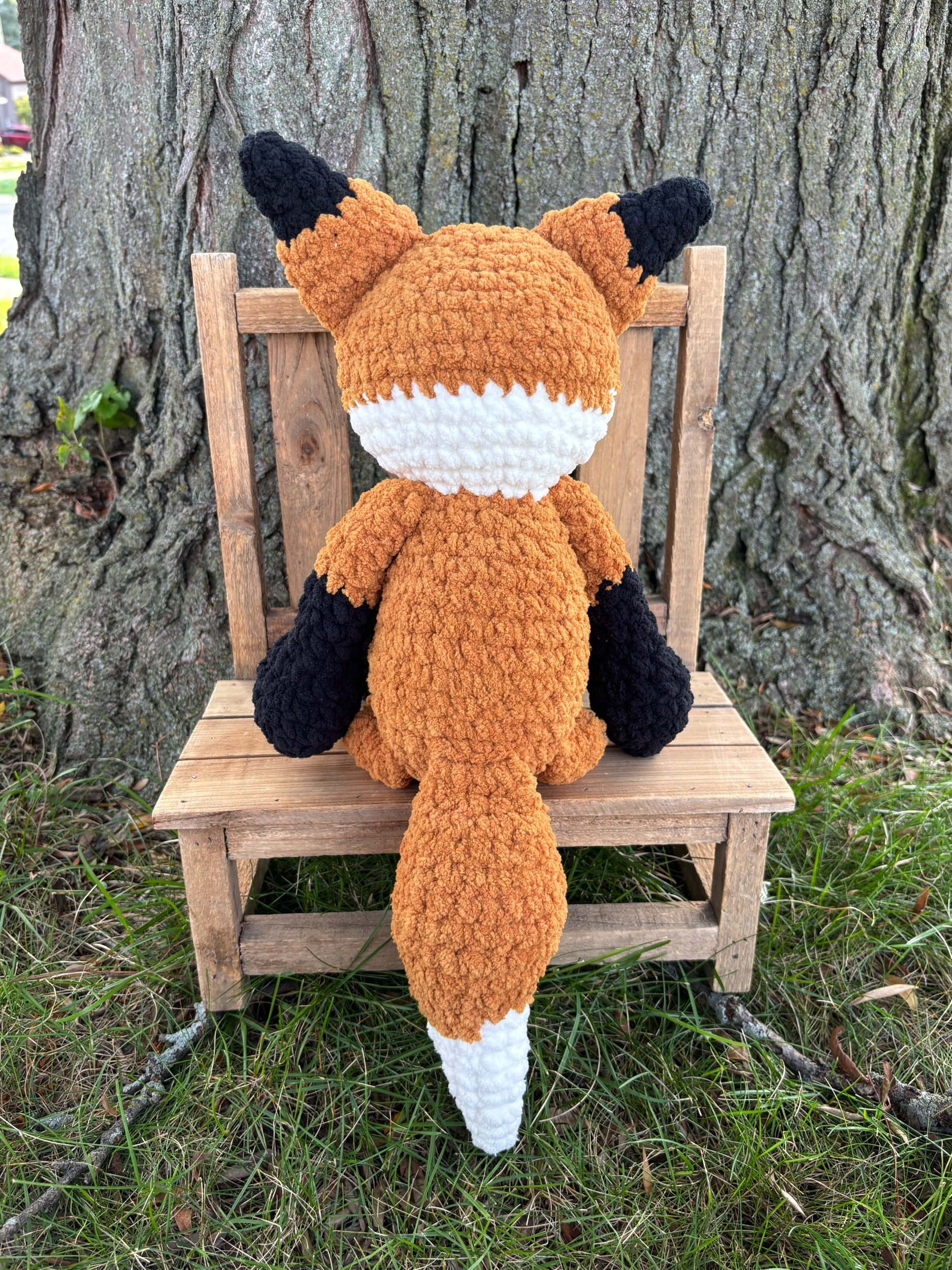 Back view of handmade crochet fox plushie showing black ears and white tail tip