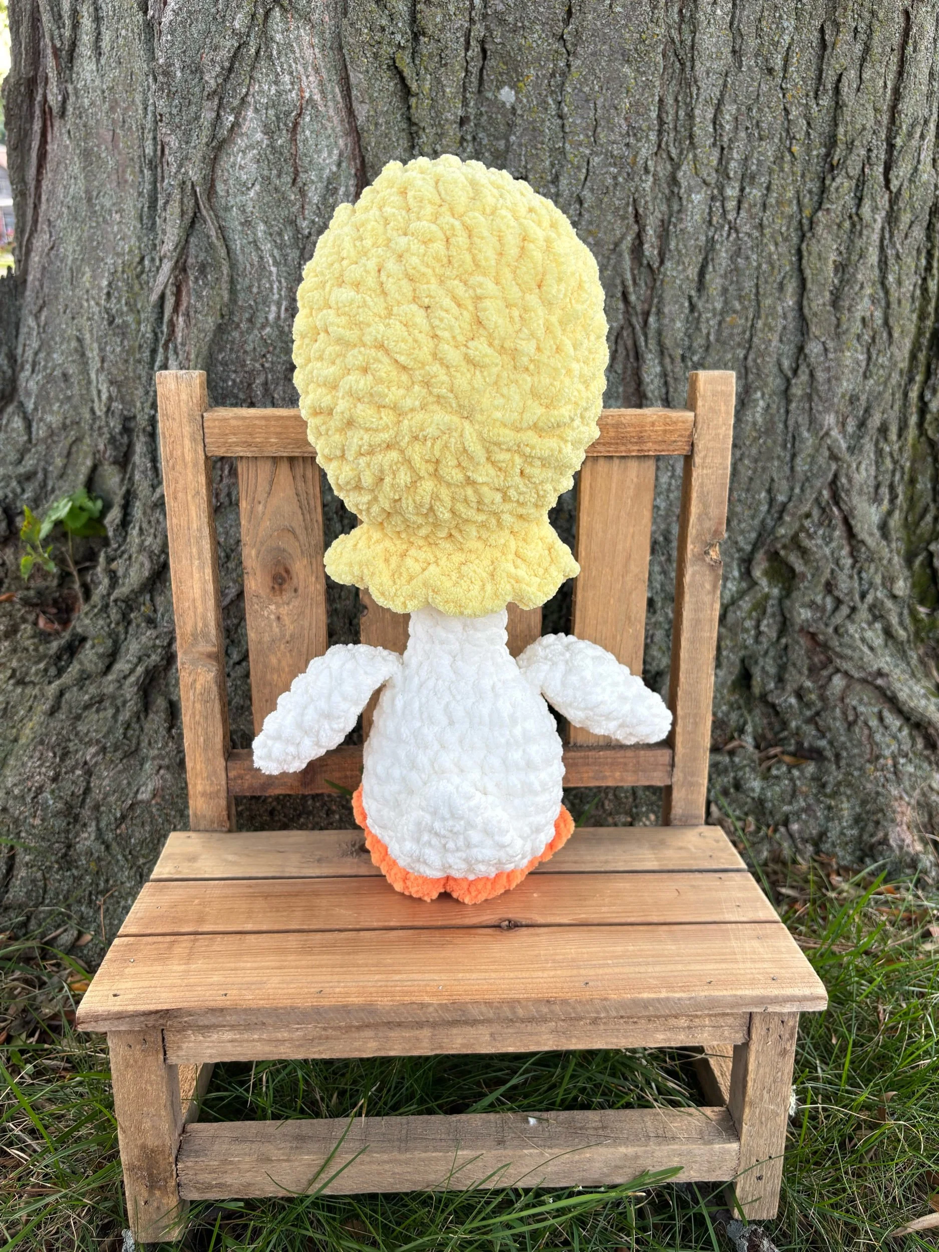 Back view of handmade crochet goose plushie showing yellow bonnet ties