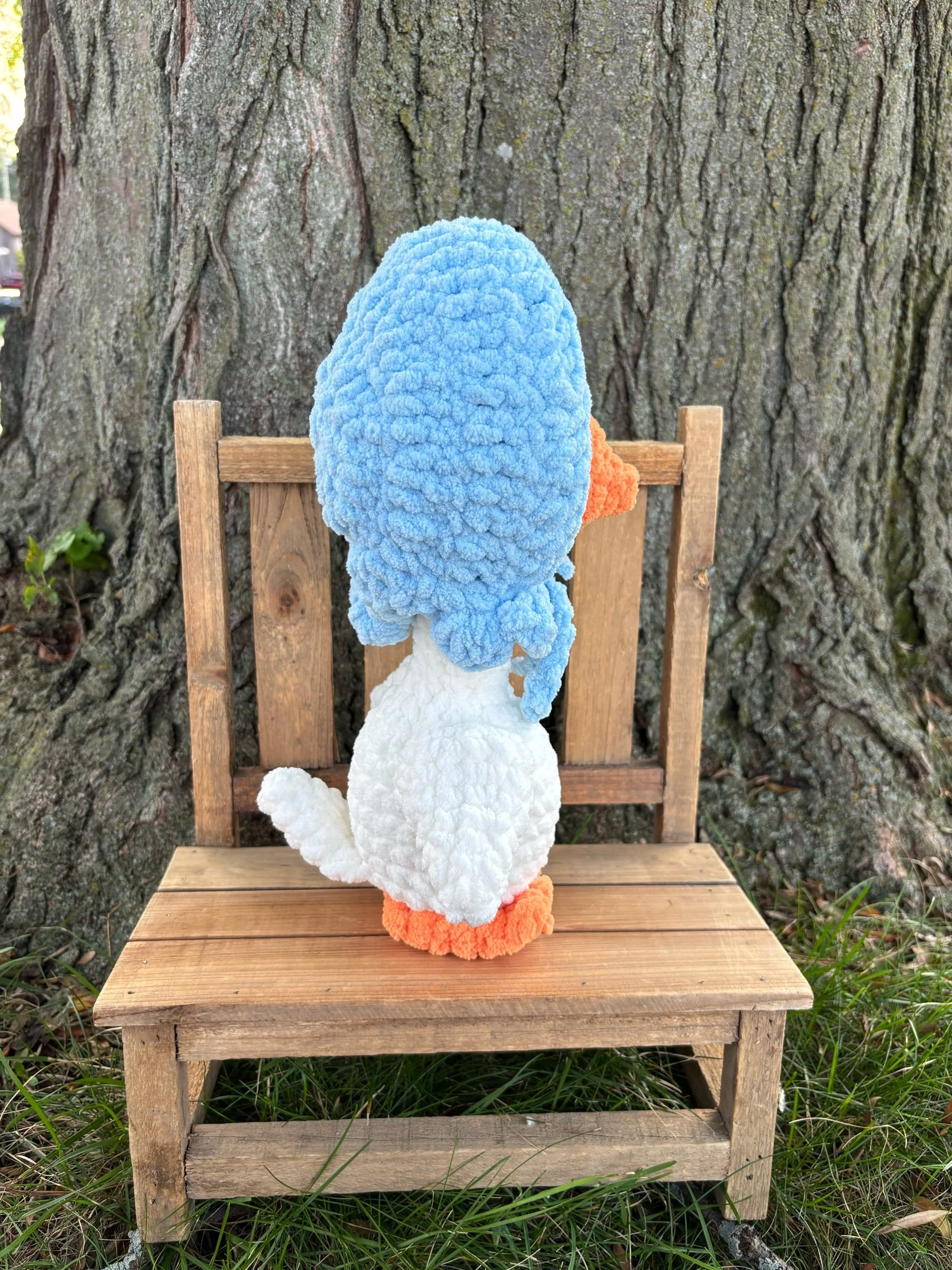 Back view of handmade crochet goose plushie showing blue bonnet ties