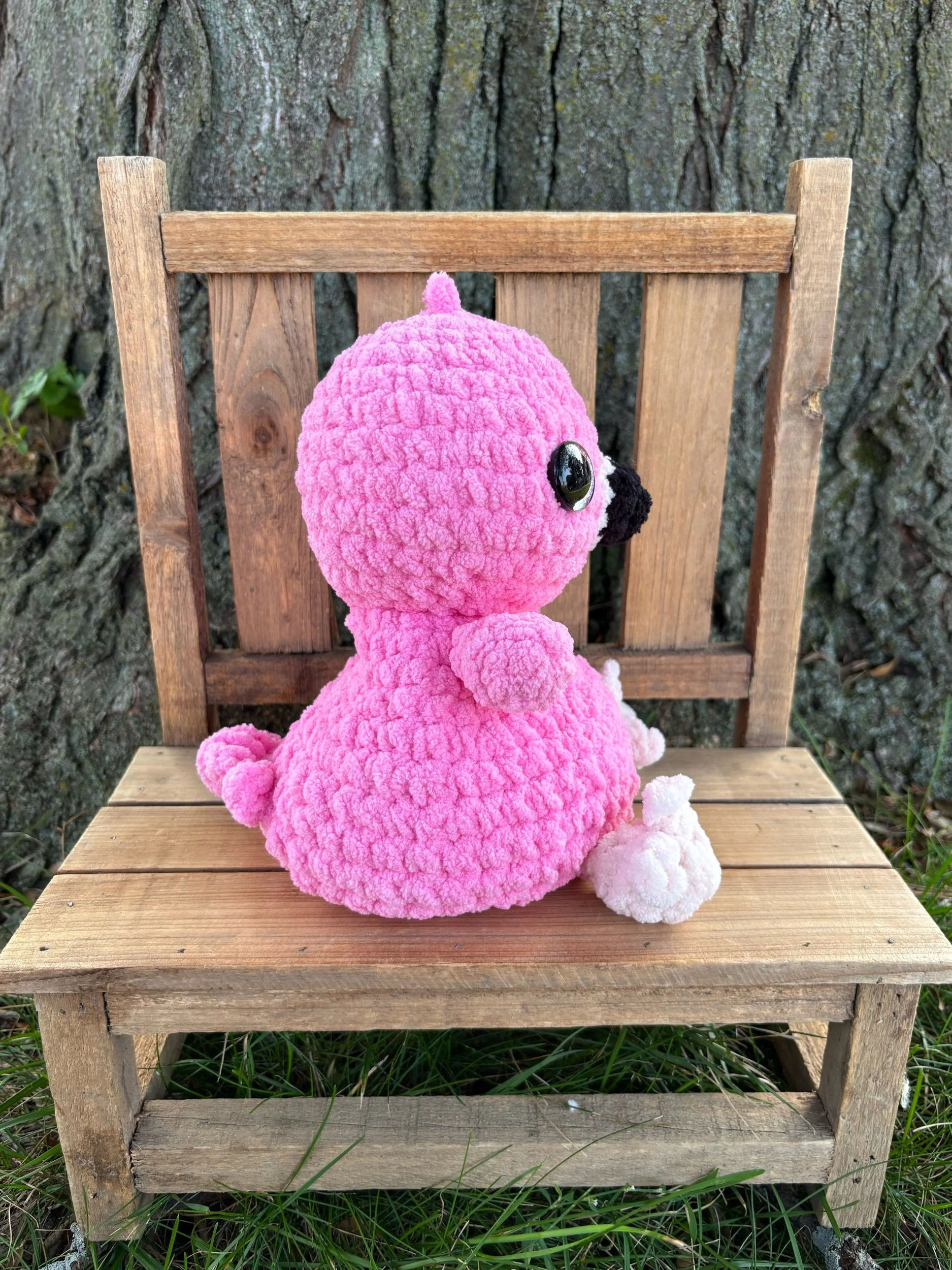 Side view of handmade weighted crochet flamingo plushie showing wing and pale pink feet