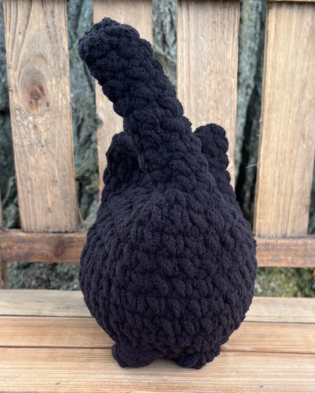 Crochet solid cat plushie sitting on wooden bench outdoors