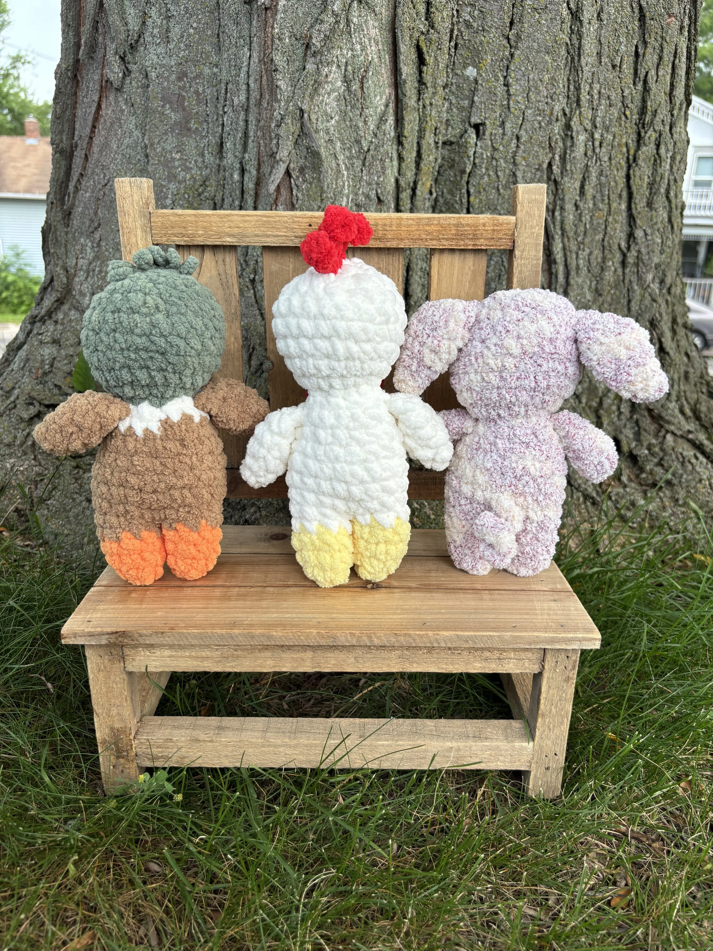 Crochet farm animal plushie bundle sitting on wooden bench outdoors