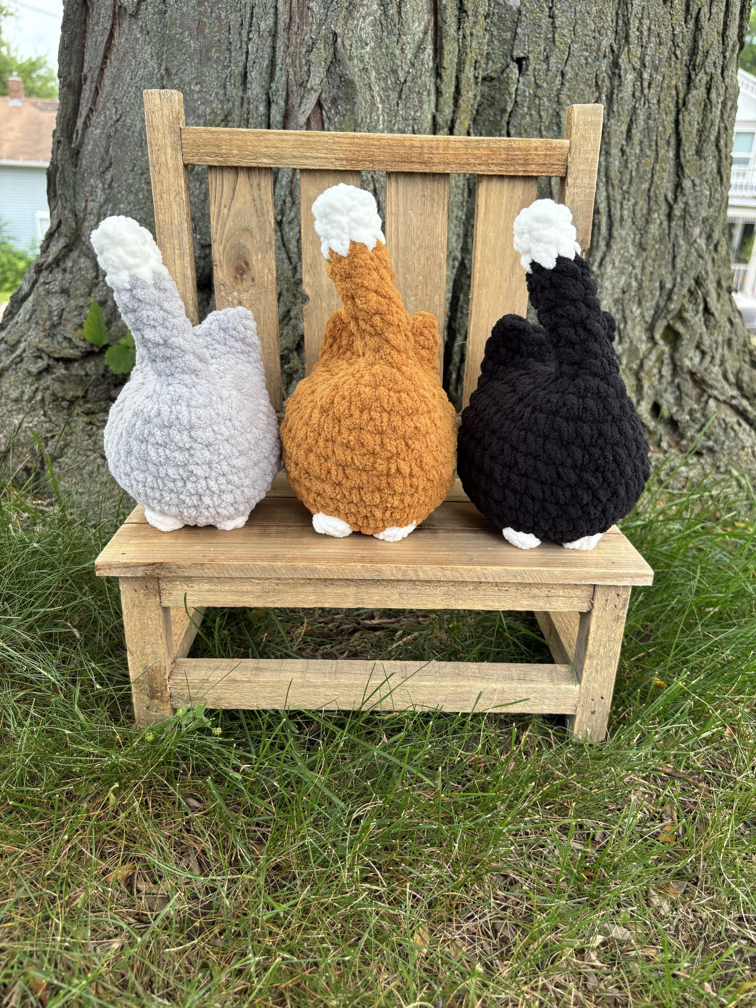 Crochet tuxedo cat plushies in grey, orange, and black on wooden bench