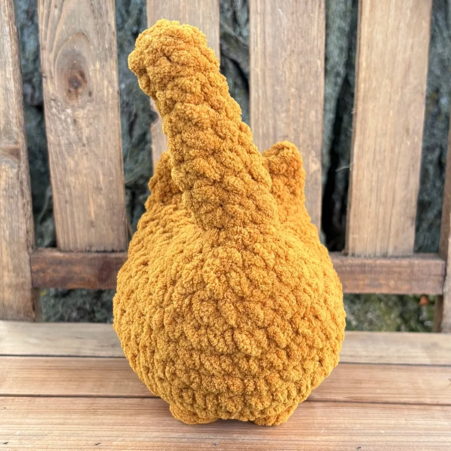 Crochet solid cat plushie sitting on wooden bench outdoors