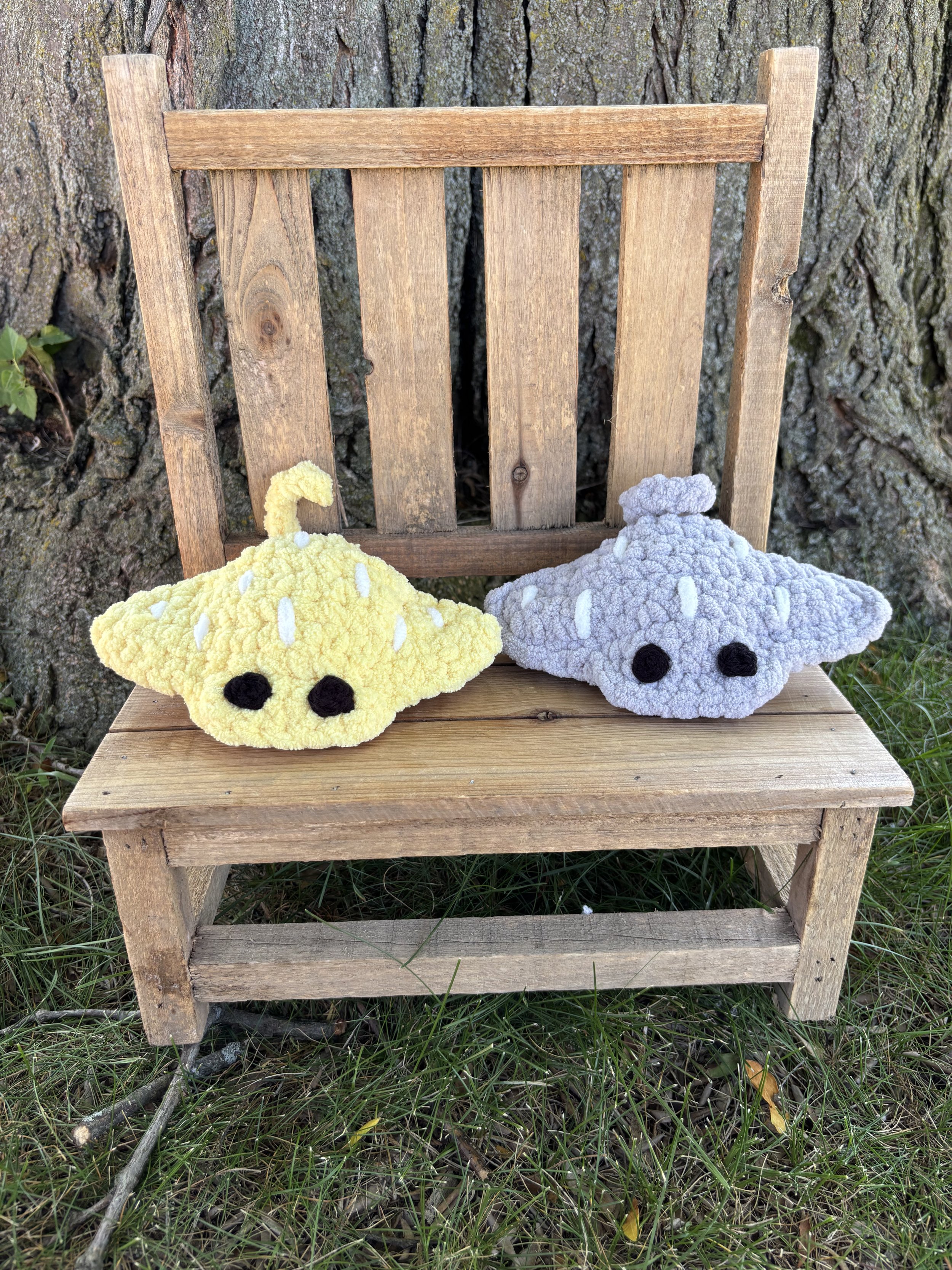 Three crochet stingray plushies in grey and yellow on wooden bench