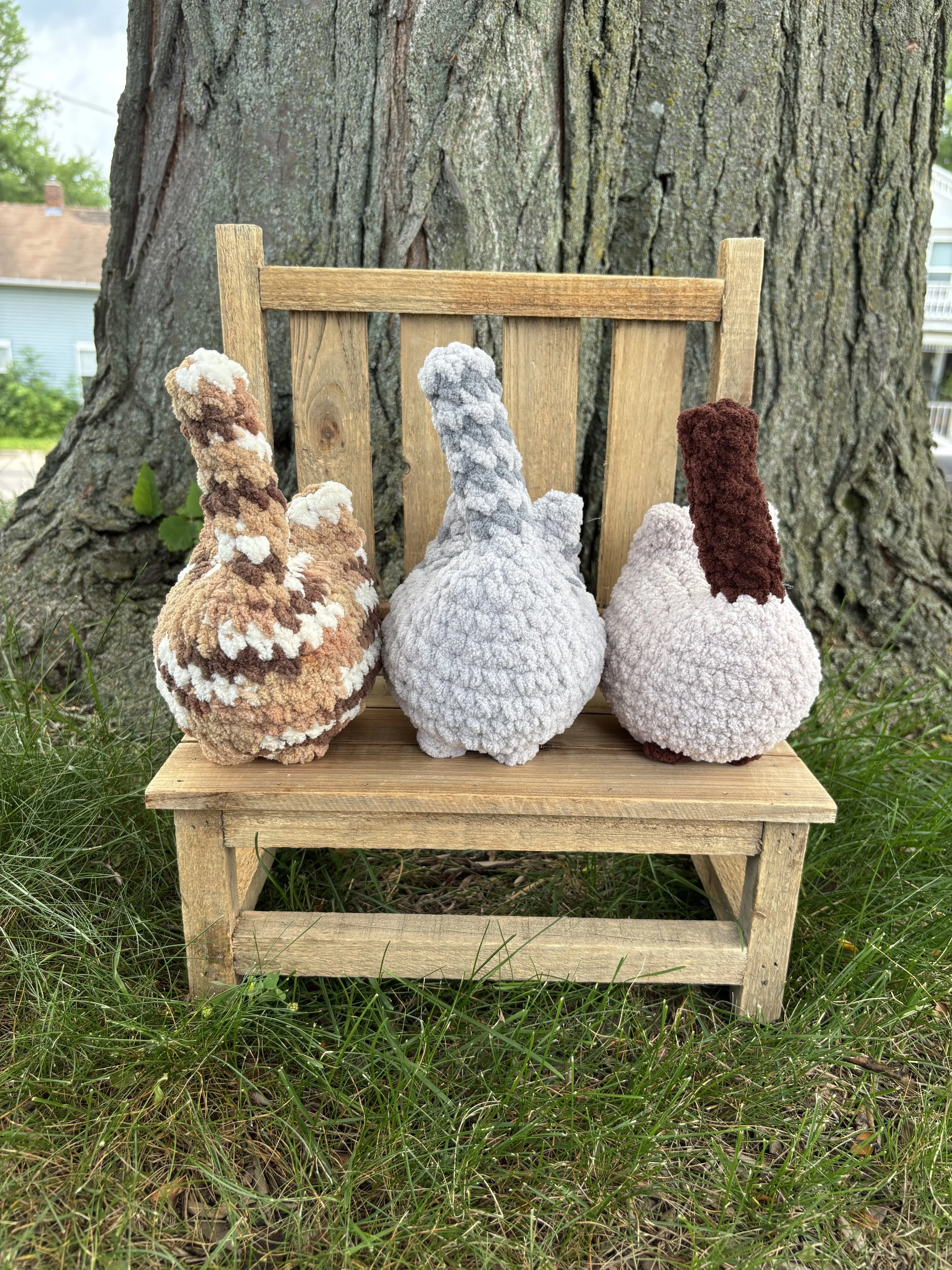 Crochet tabby and Siamese cat plushies sitting on wooden bench outdoors