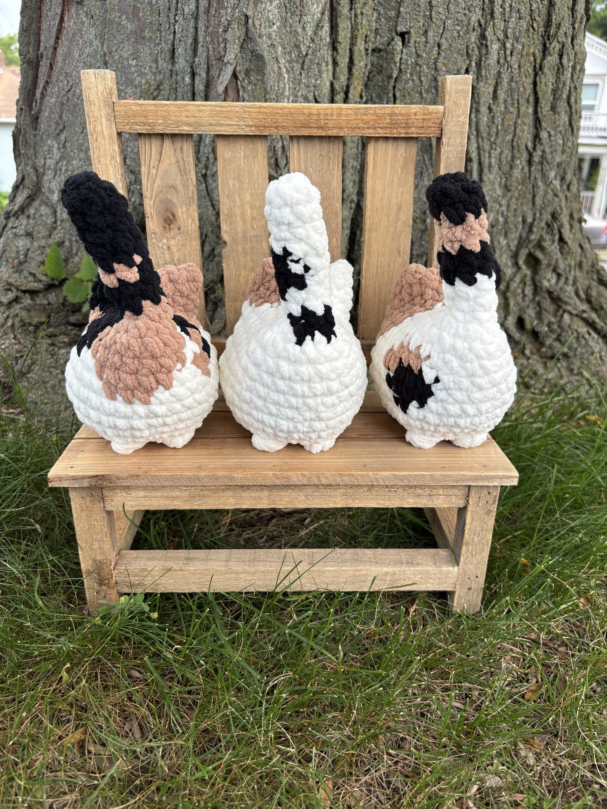 Three crochet calico cat plushies with different patterns on wooden bench