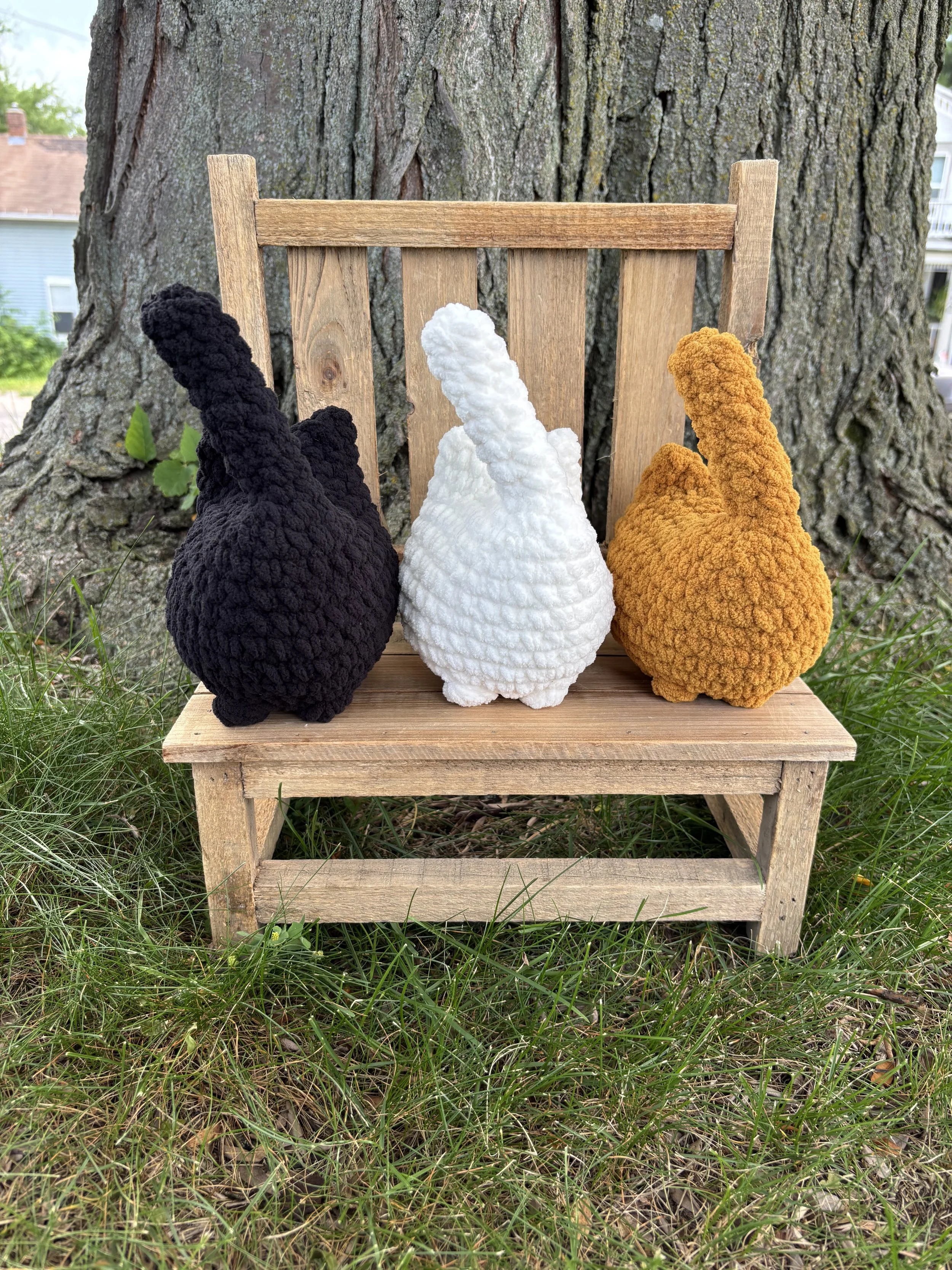 Crochet solid cat plushie sitting on wooden bench outdoors