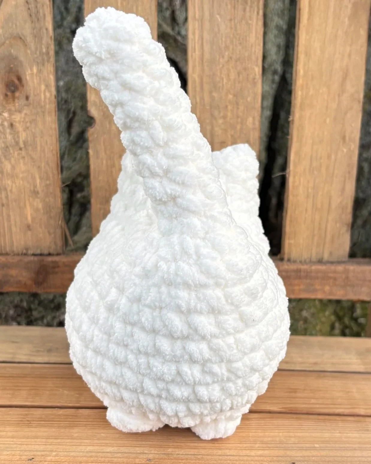 Crochet solid cat plushie sitting on wooden bench outdoors