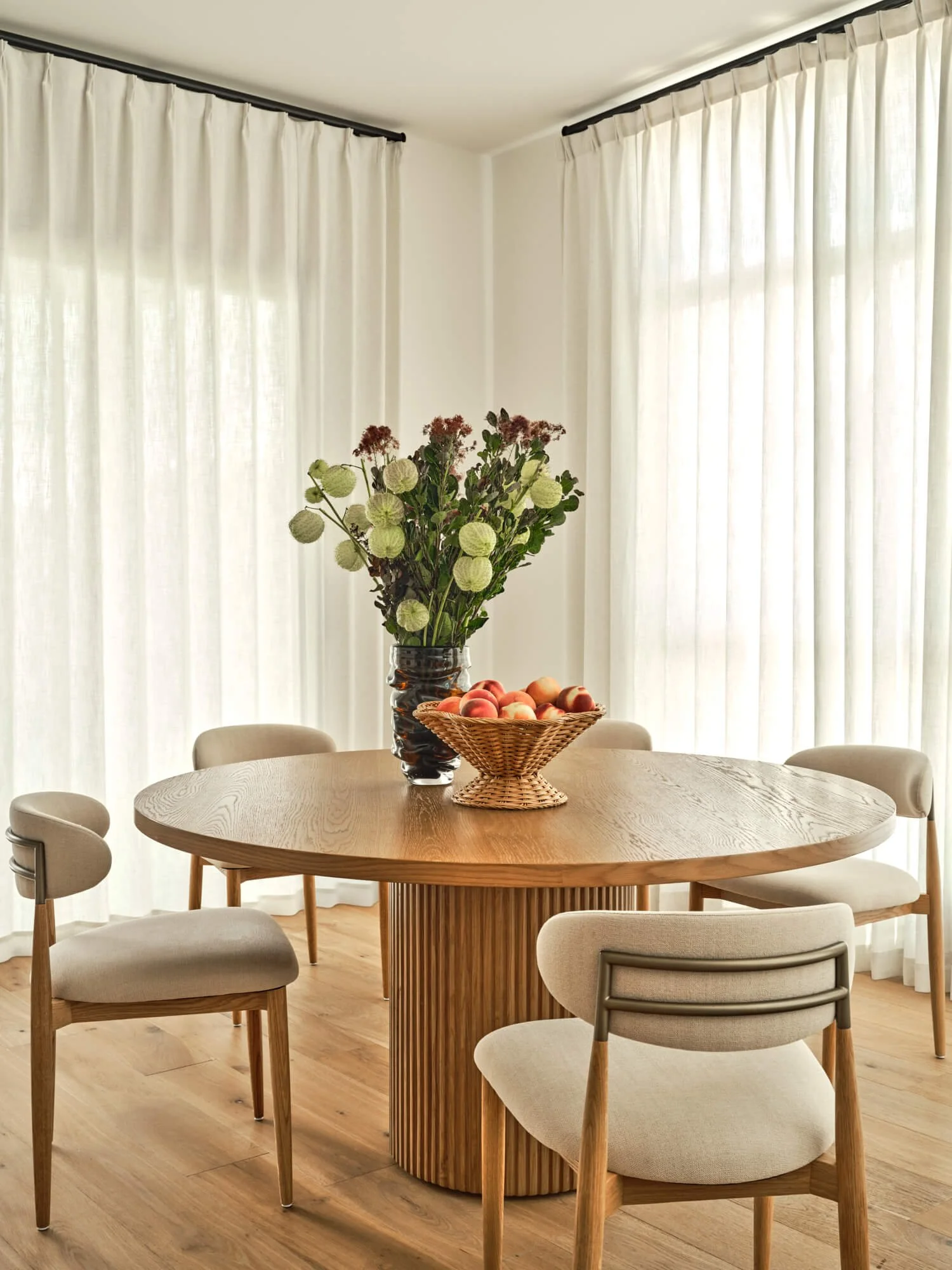 Natural round wood dining table paired with neutral cream fabric chair with brass details