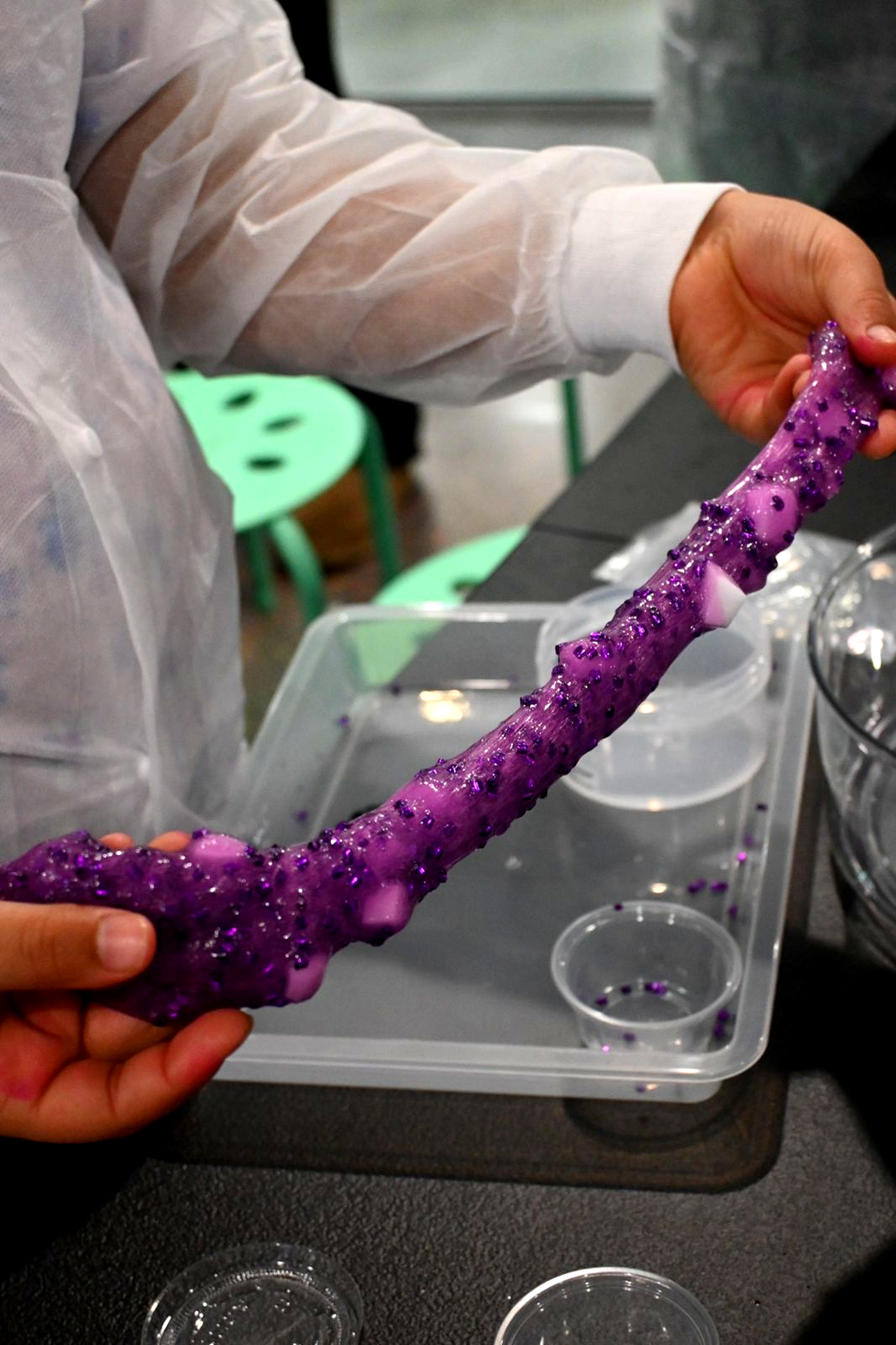 Person holding a purple slime with add-ins, stretching it out, in a slime laboratory.