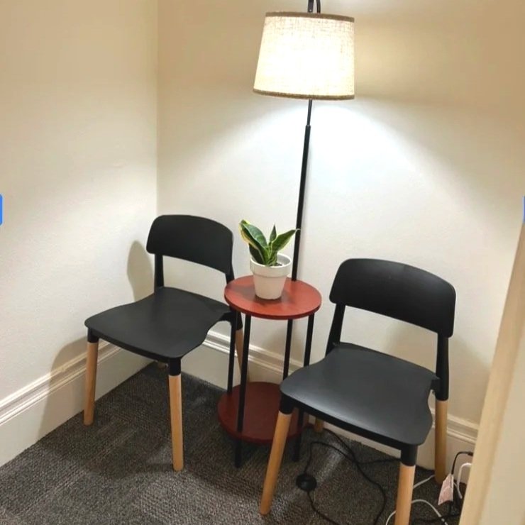 Therapy waiting room with 2 black chairs, lamp, small side table, and plant