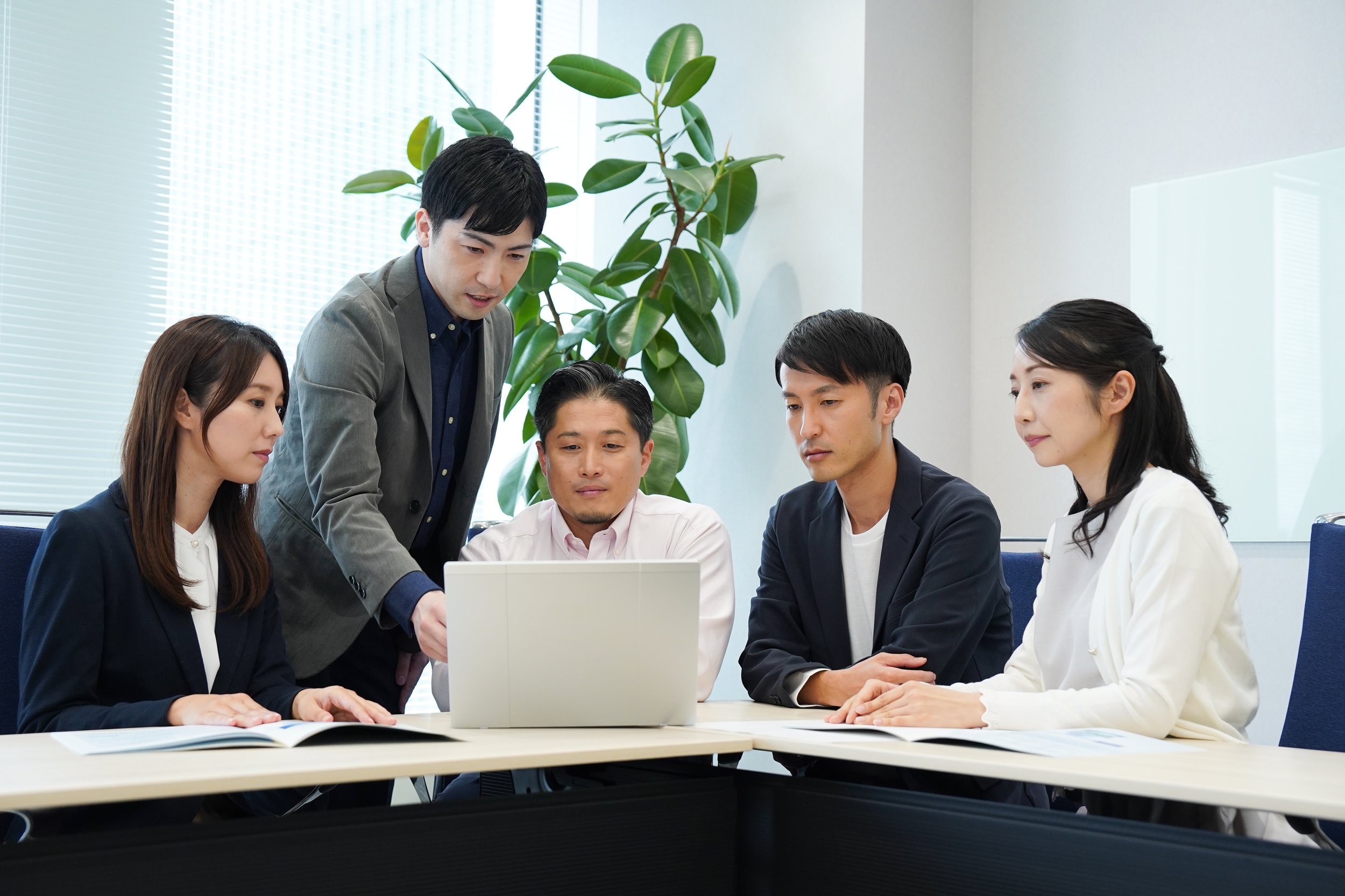Five professionals having a meeting around a laptop in an office conference room.