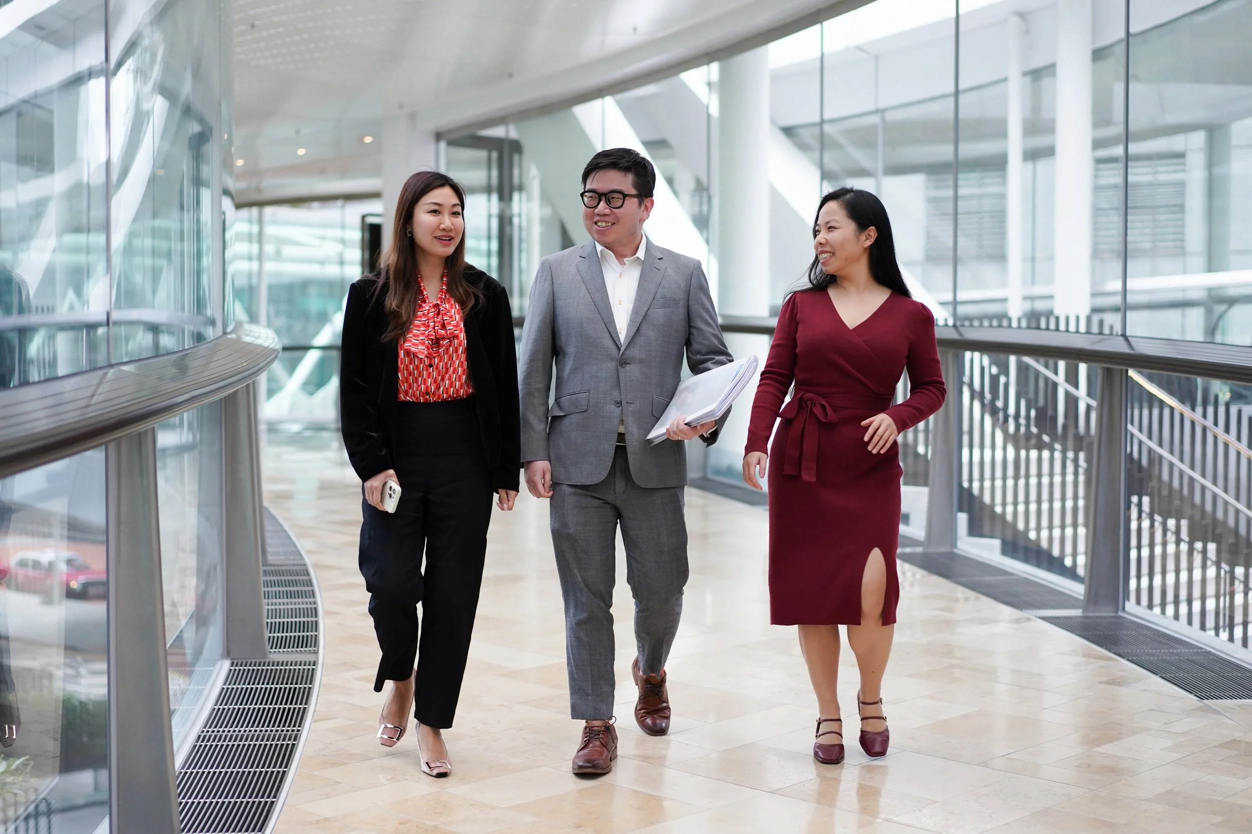 Three diverse business professionals walking and talking in a modern office building corridor.