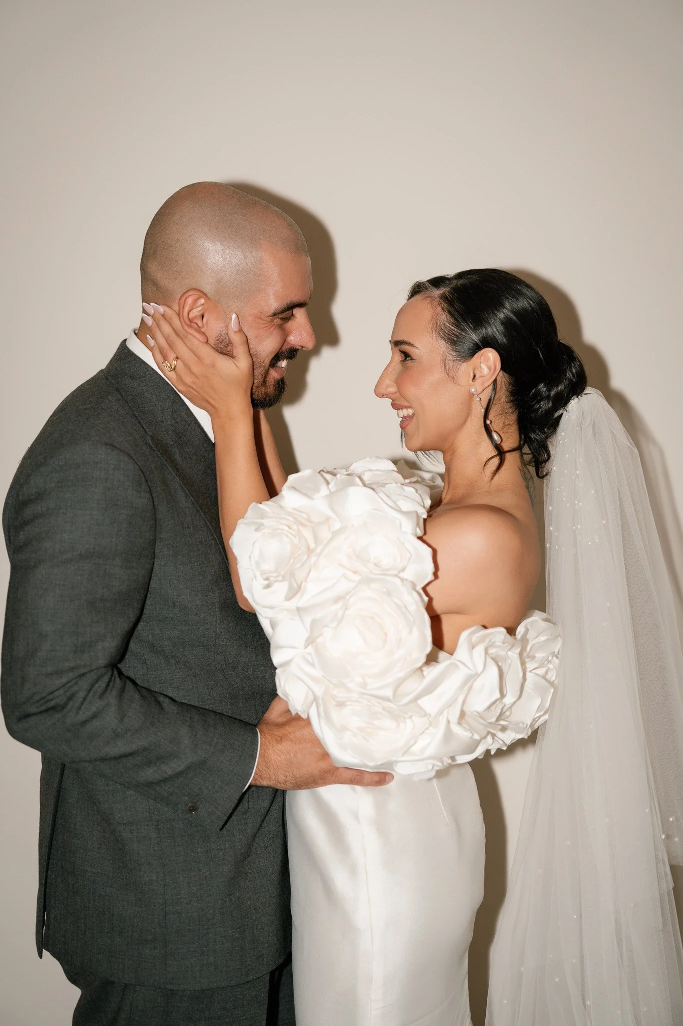 A bride and groom in wedding attire sharing a joyful moment, holding each other close and smiling, with the bride's hand on the groom's face.