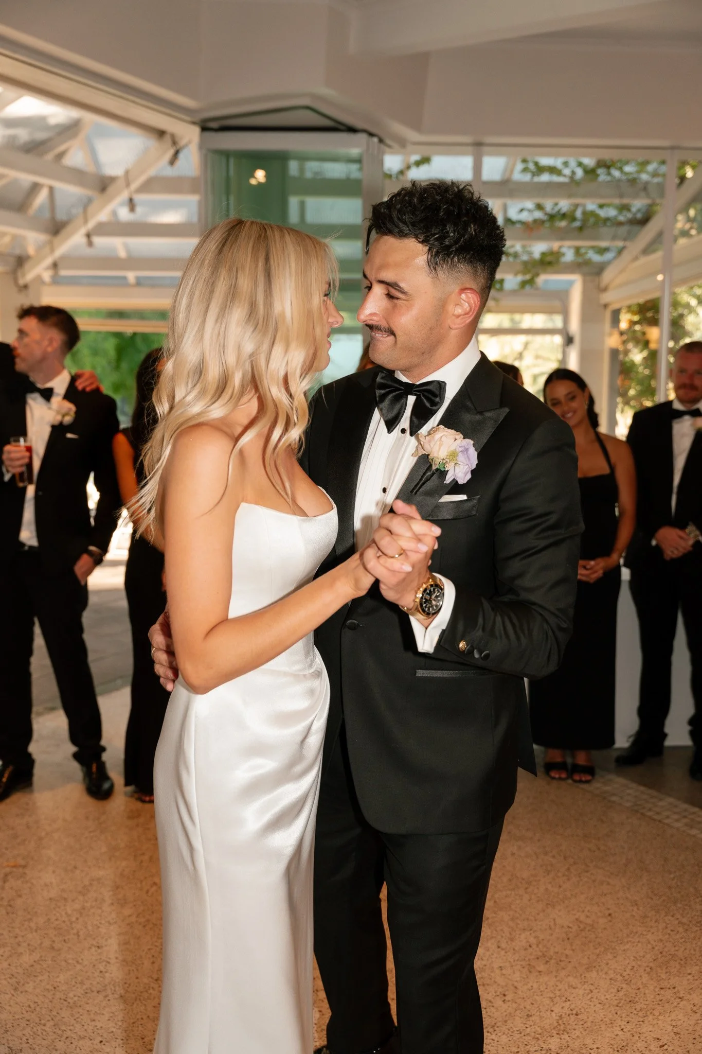 A bride and groom dance closely during their wedding reception, surrounded by guests in formal attire.