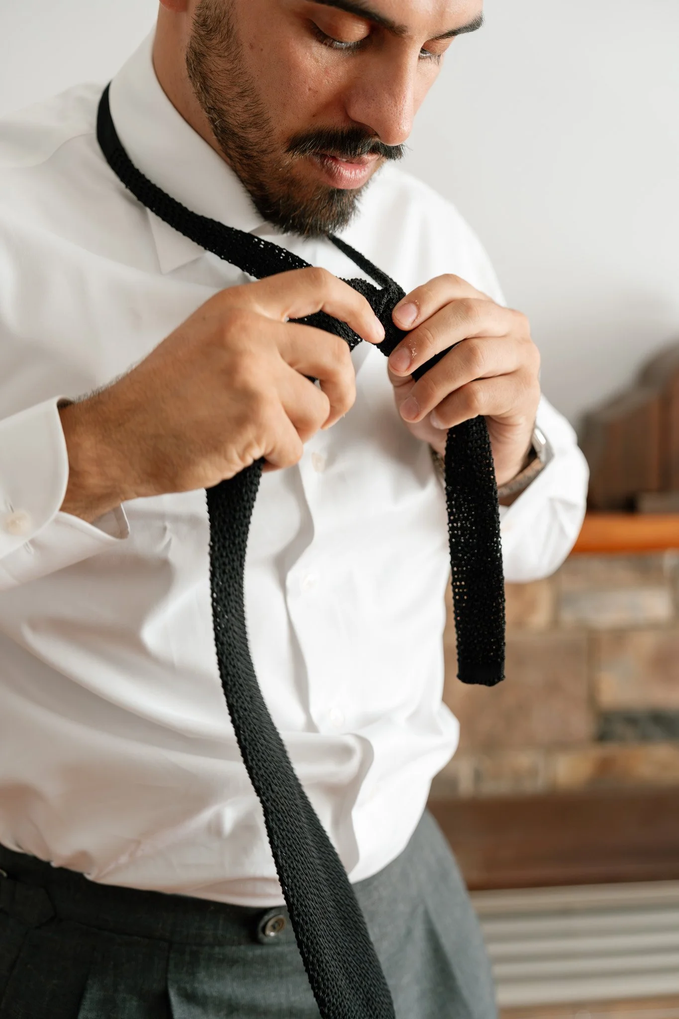 A man in a white dress shirt ties a black necktie.