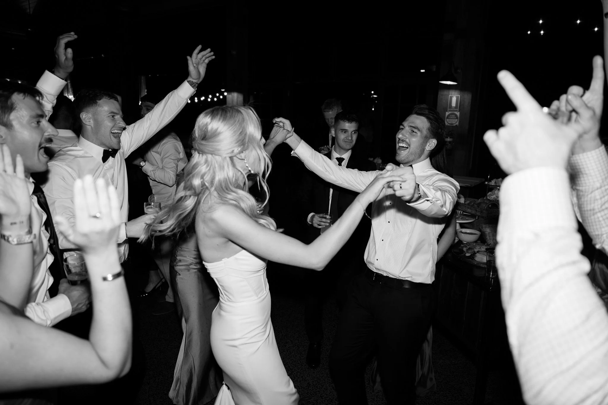 People dancing and celebrating at a party or wedding reception, smiling and holding hands.