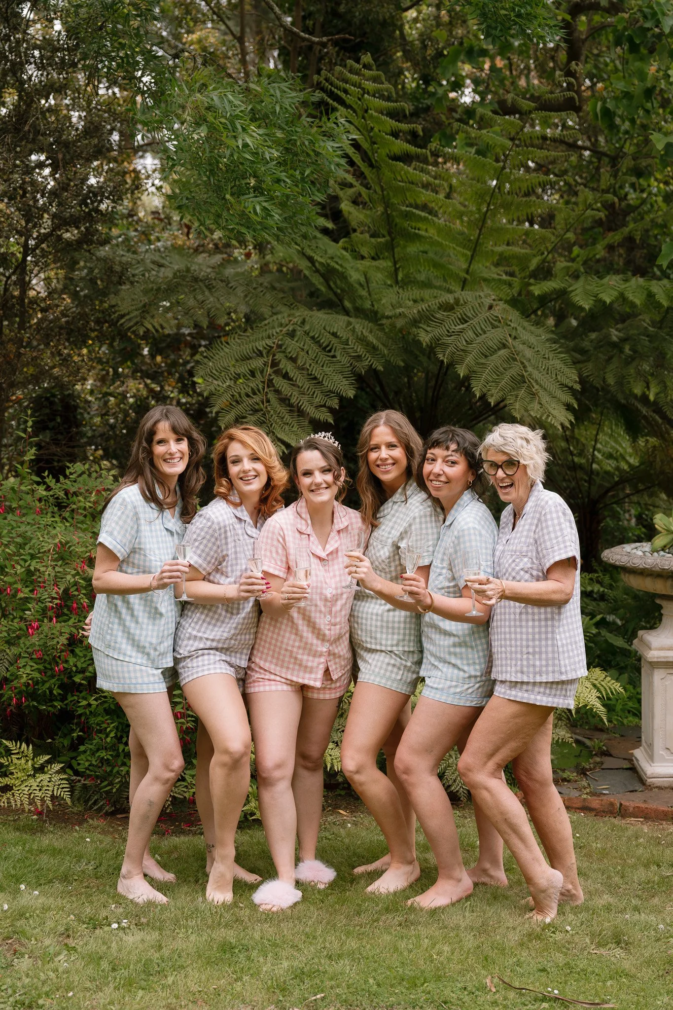 Six women in pajamas holding champagne glasses in a garden.