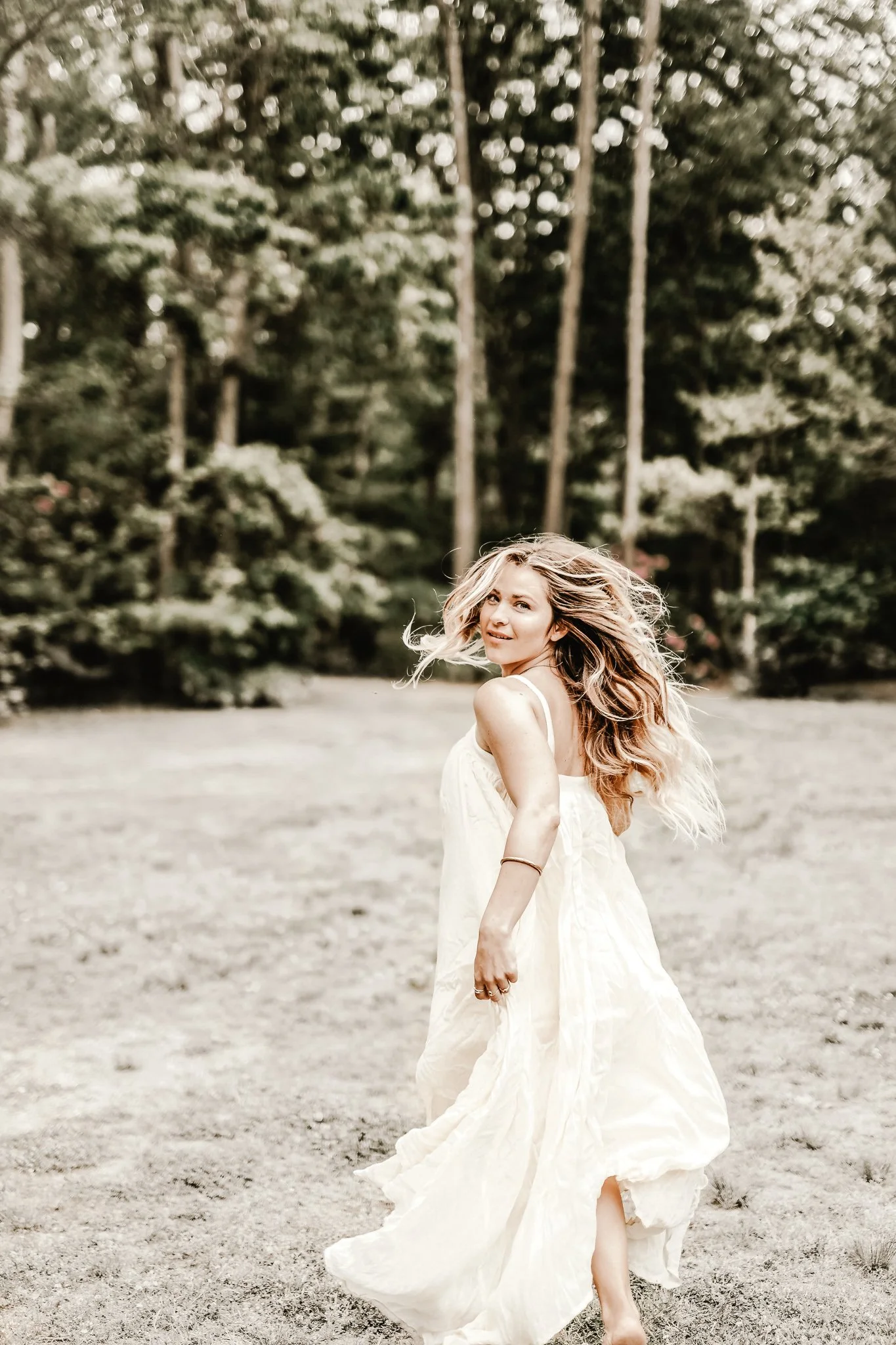 Woman in a white dress twirling outdoors with trees in the background.