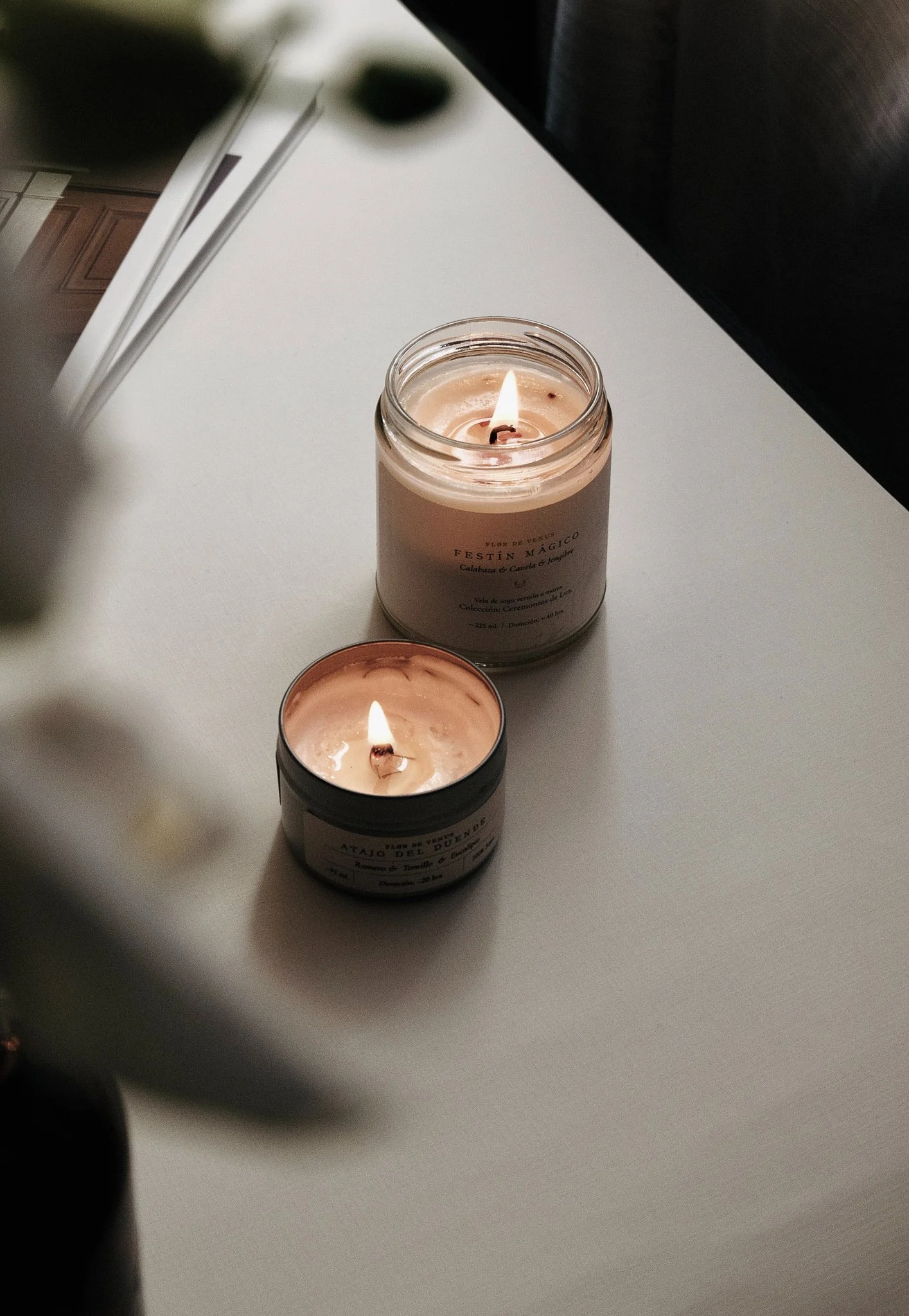 Two lit candles on a white table next to an open magazine.