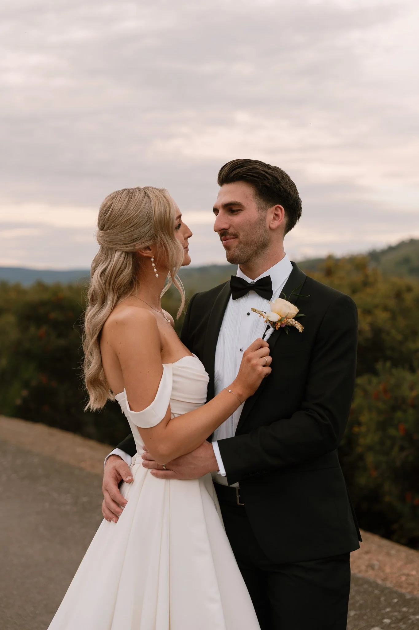 A bride and groom in wedding attire standing outdoors looking at each other.