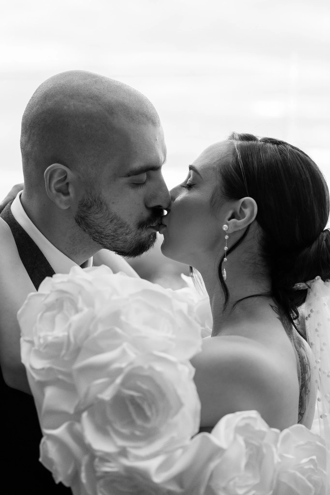 Black and white photo of a bride and groom kissing, with large white floral decorations in the foreground.