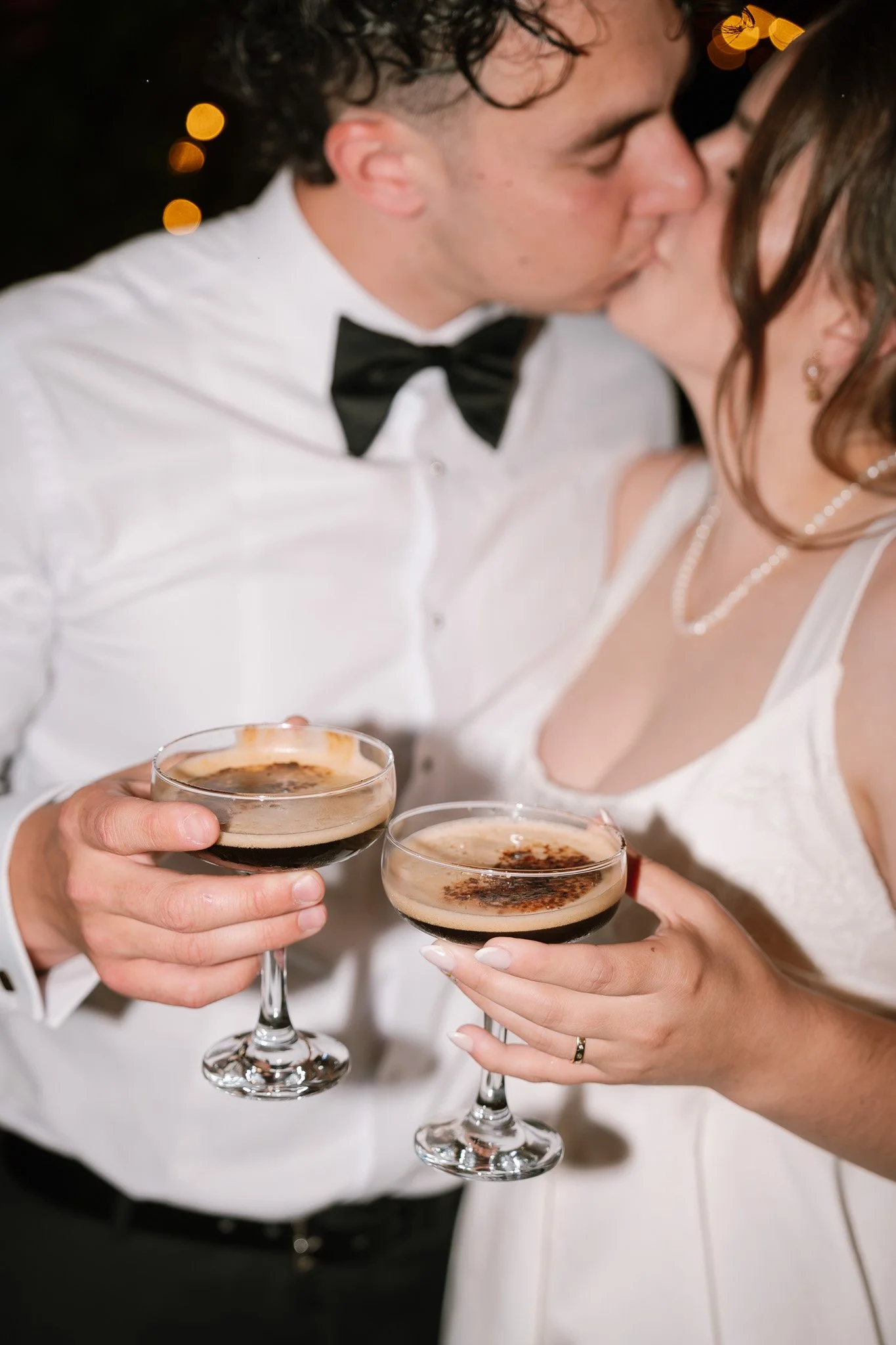 A couple kissing while holding glasses of dark beer or stout during a celebration.