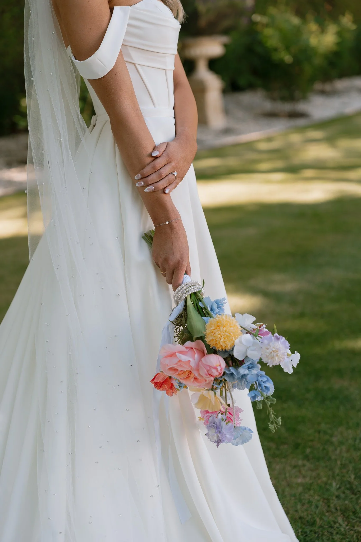 Bride wearing a white wedding dress holding a colorful bouquet of flowers outdoors.