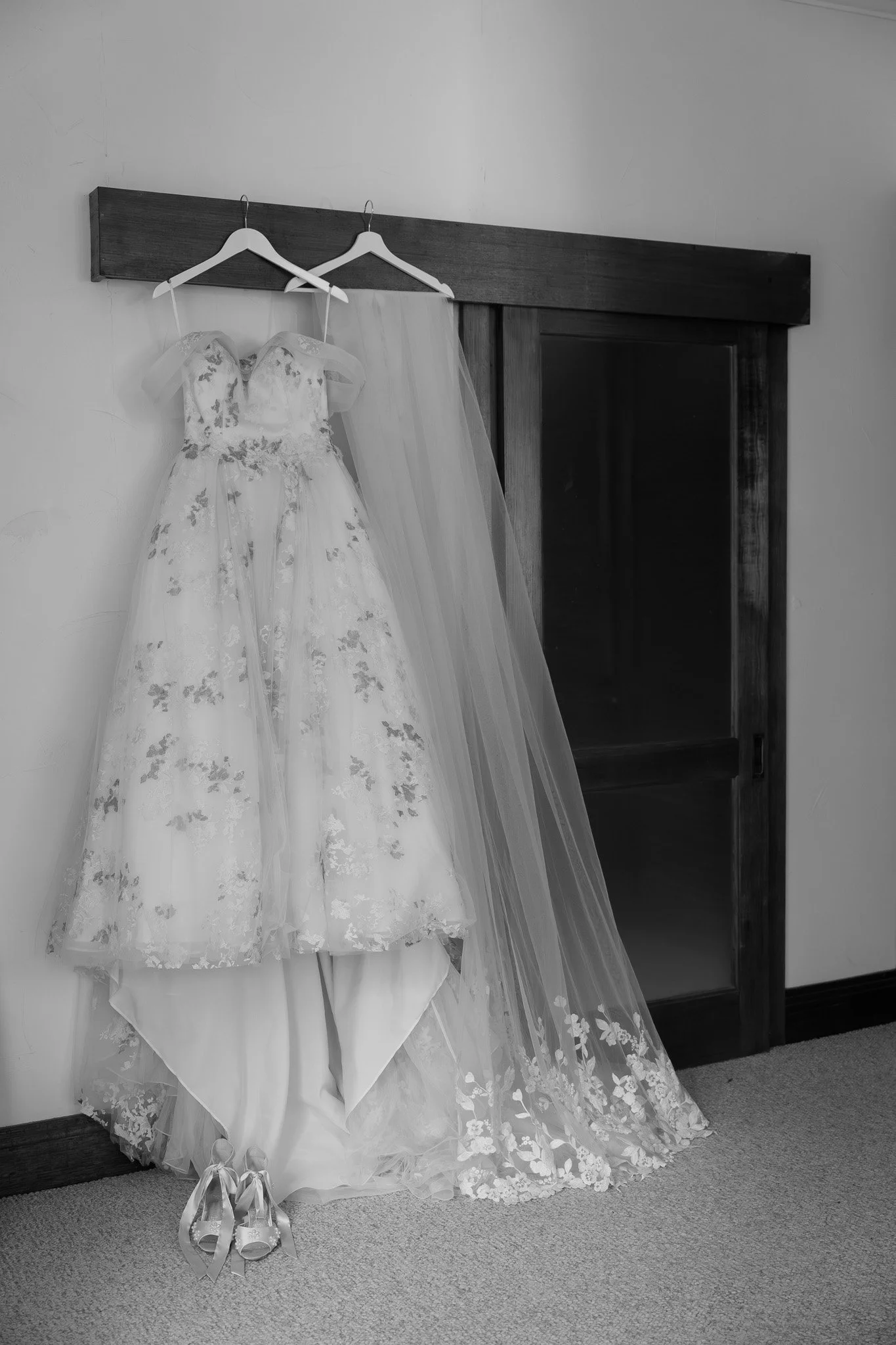 A wedding dress and veil hung on hangers against a wall near a wooden sliding door.