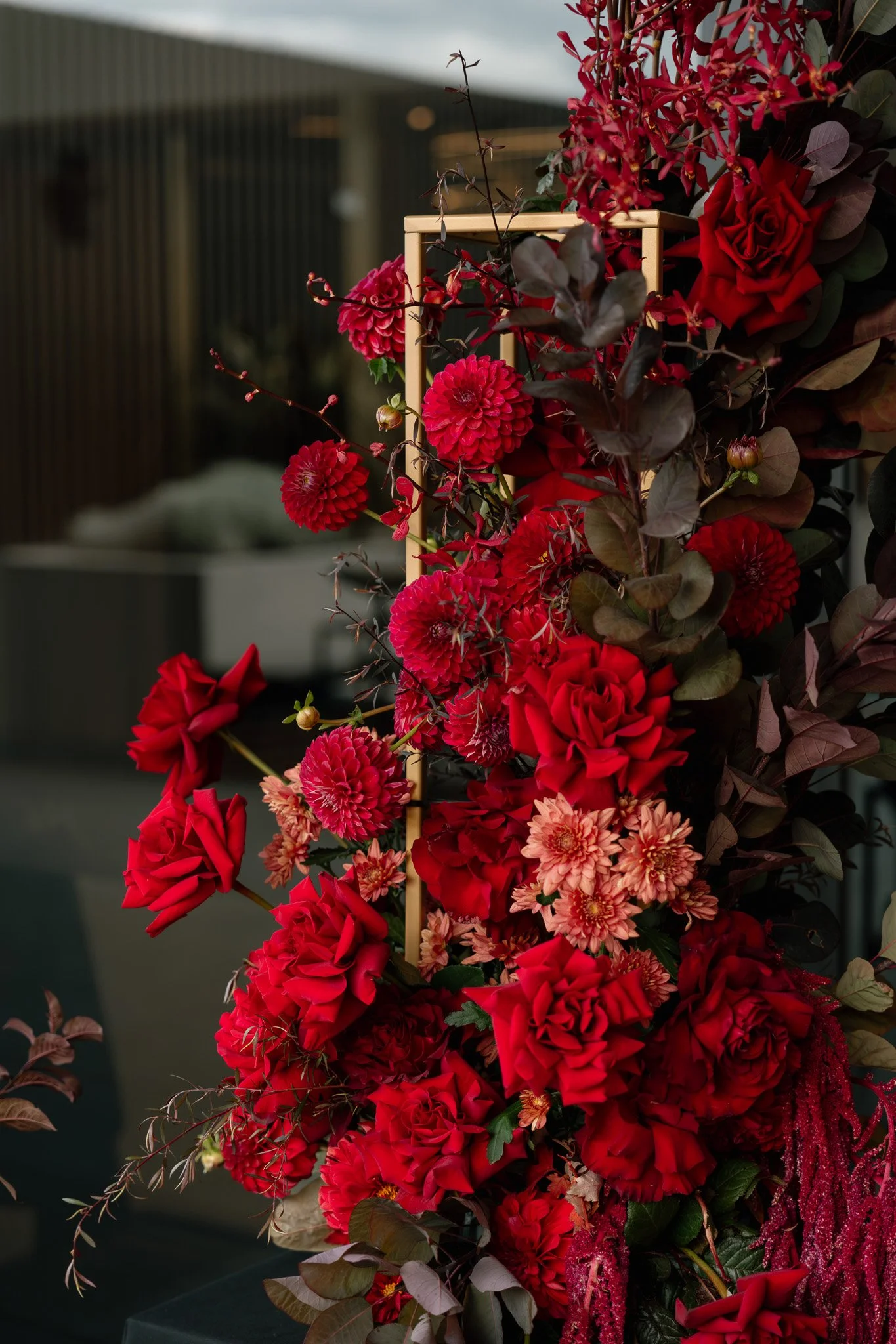 Red floral arrangement with various flowers including roses and dahlias, accented with dark foliage.