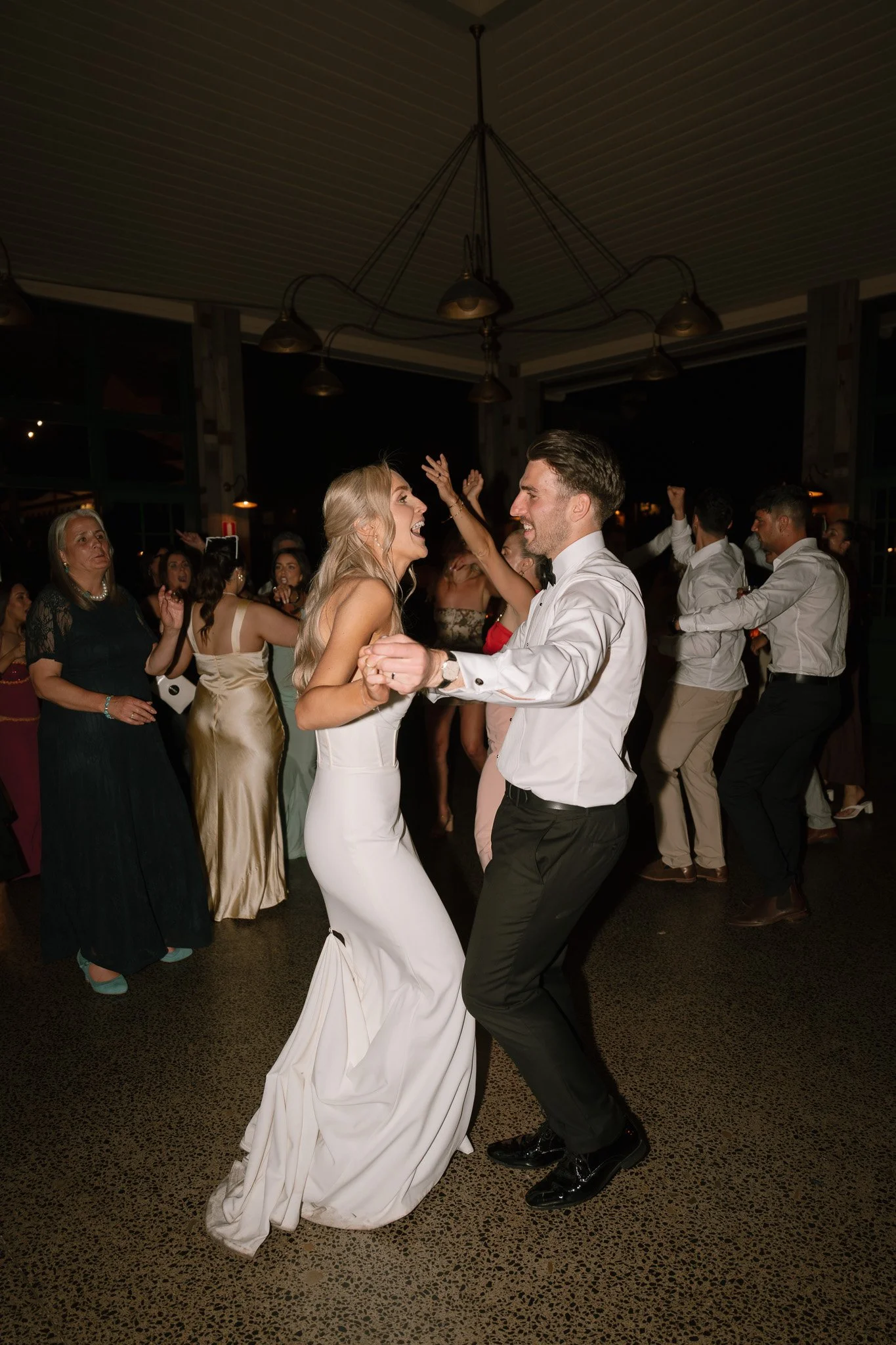 Bride and groom dancing at a wedding reception, surrounded by guests enjoying the celebration.