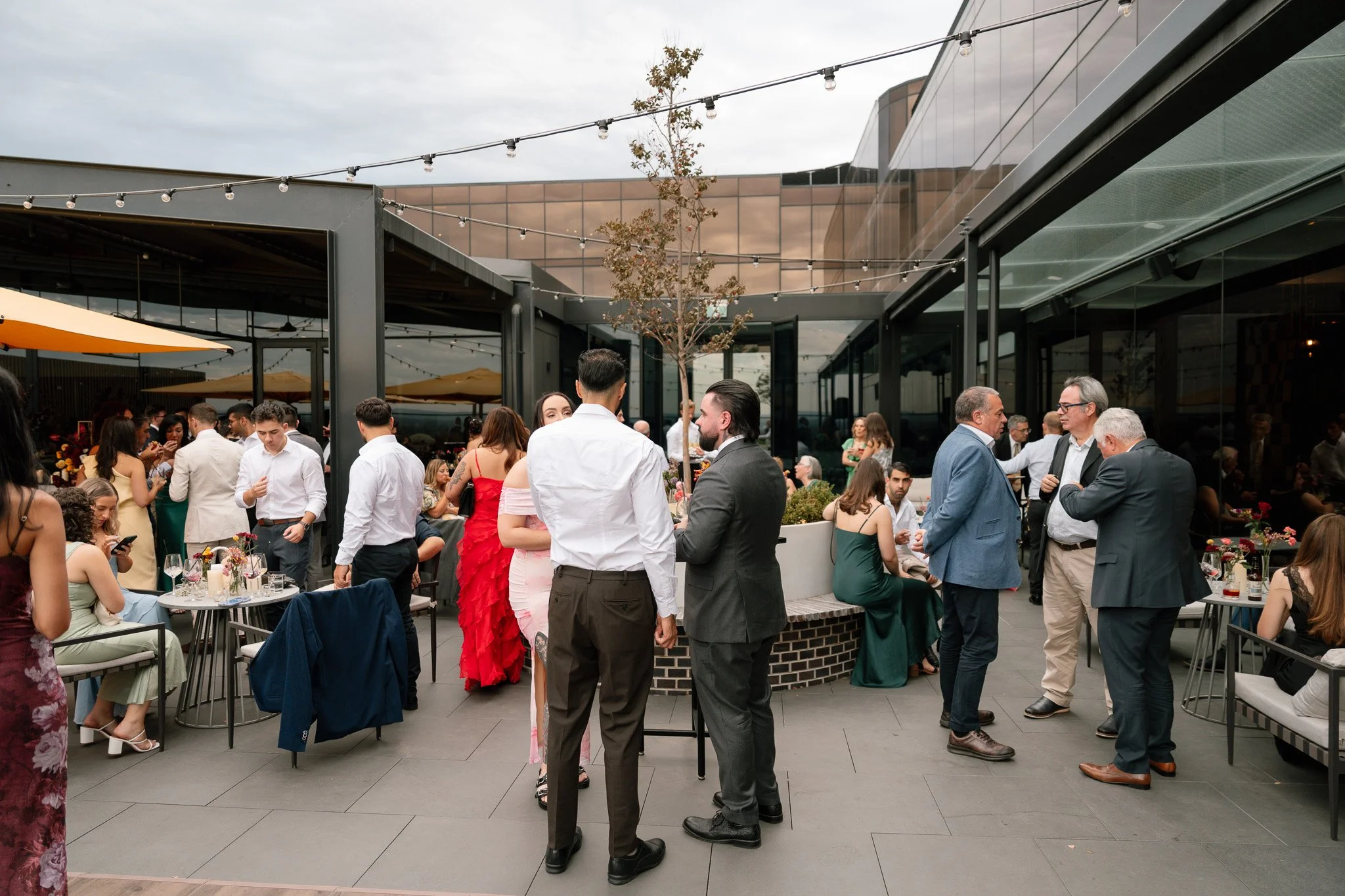 People socializing at a rooftop gathering during the evening with string lights and modern outdoor furniture.