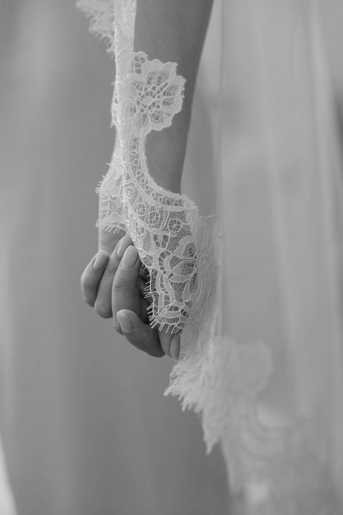 Close-up of a woman's hand holding a lace sleeve of a wedding dress.