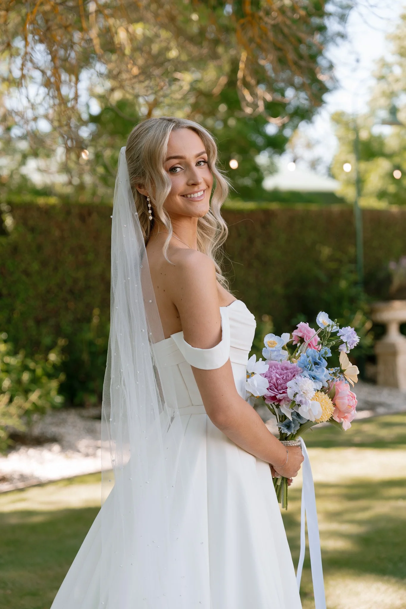 Bride in white wedding dress holding a bouquet of colorful flowers outdoors.