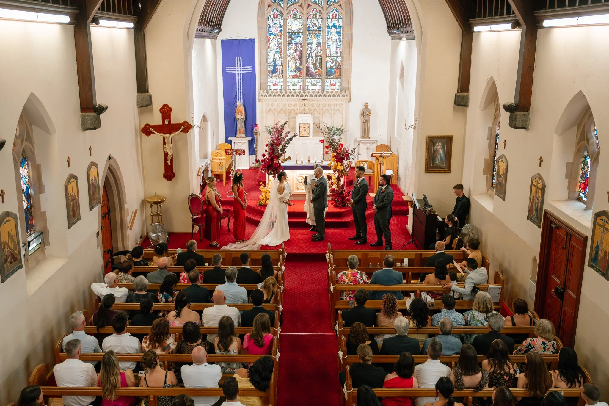 A wedding ceremony taking place inside a church with guests seated in pews, a bride and groom at the altar, and wedding party members present.