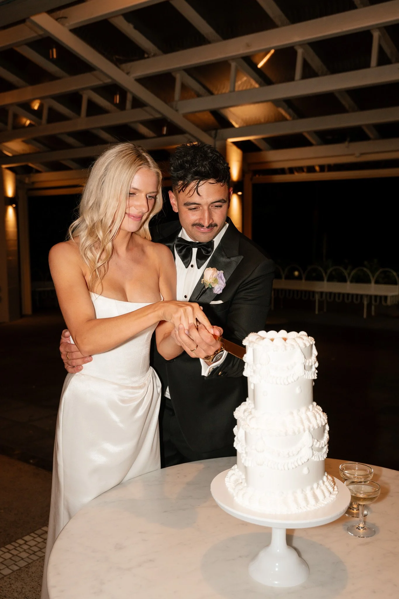 A bride and groom in formal attire cutting their wedding cake together at a reception.