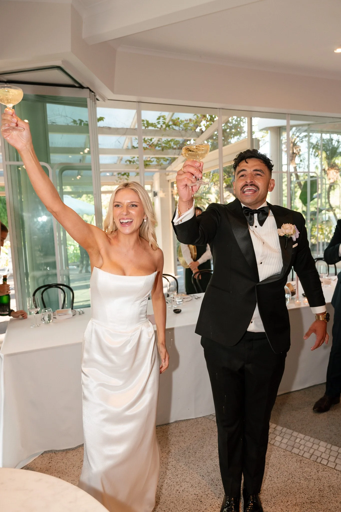 A bride and groom celebrating with champagne glasses at their wedding reception, smiling and raising their glasses in toast.