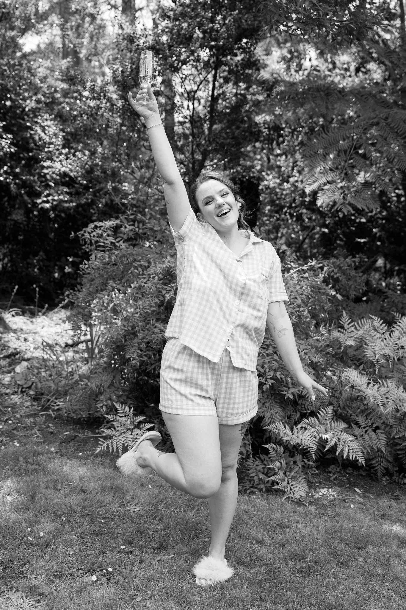 A woman in pajamas holding a glass of champagne and celebrating outdoors.