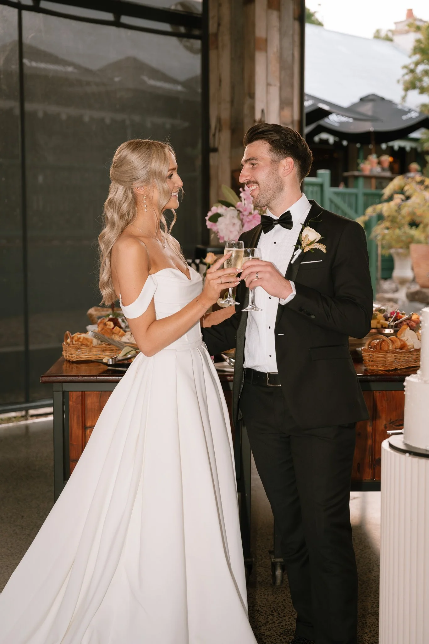 A bride and groom toast with champagne at their wedding reception, smiling and looking at each other.