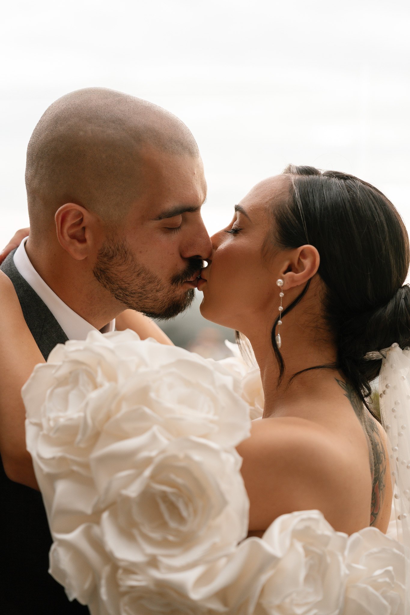 A bride and groom kissing, in wedding attire, with white roses in the foreground.