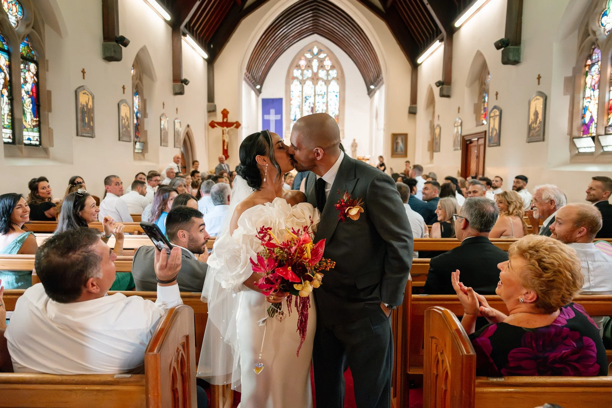 A newlywed couple sharing a kiss inside a church during their wedding ceremony, surrounded by seated guests.