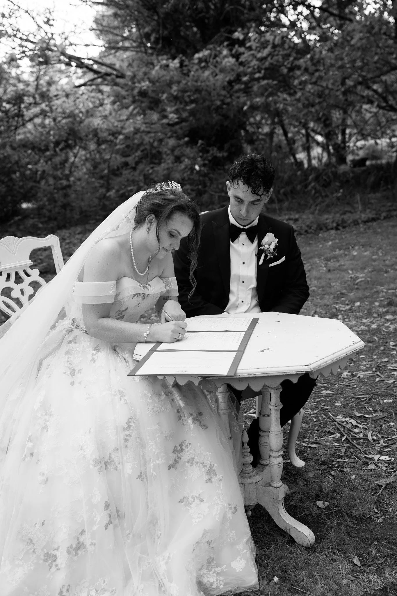 A bride and groom signing documents outdoors at a wedding ceremony.