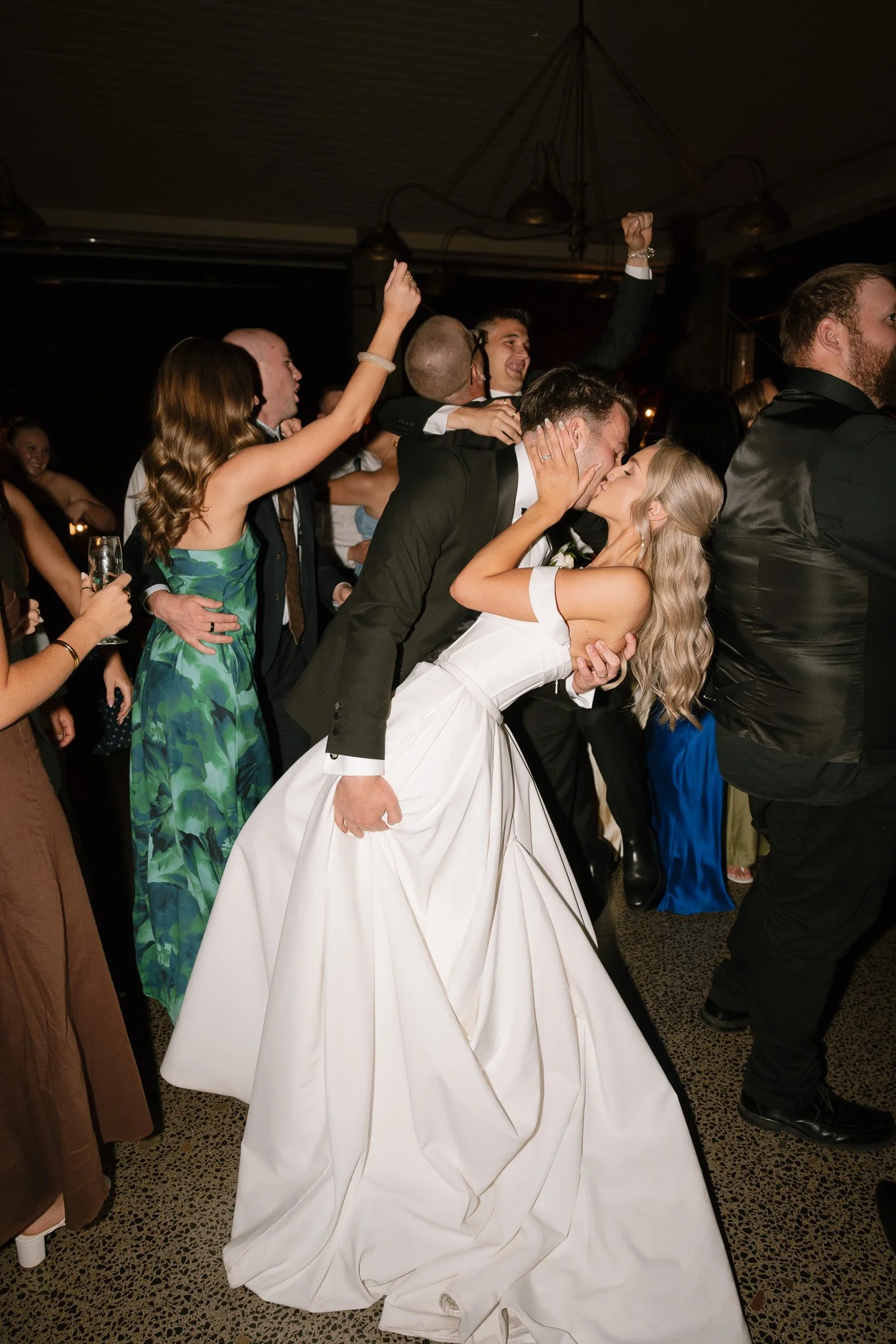 A wedding reception with the bride and groom sharing a kiss while dancing among friends and family.