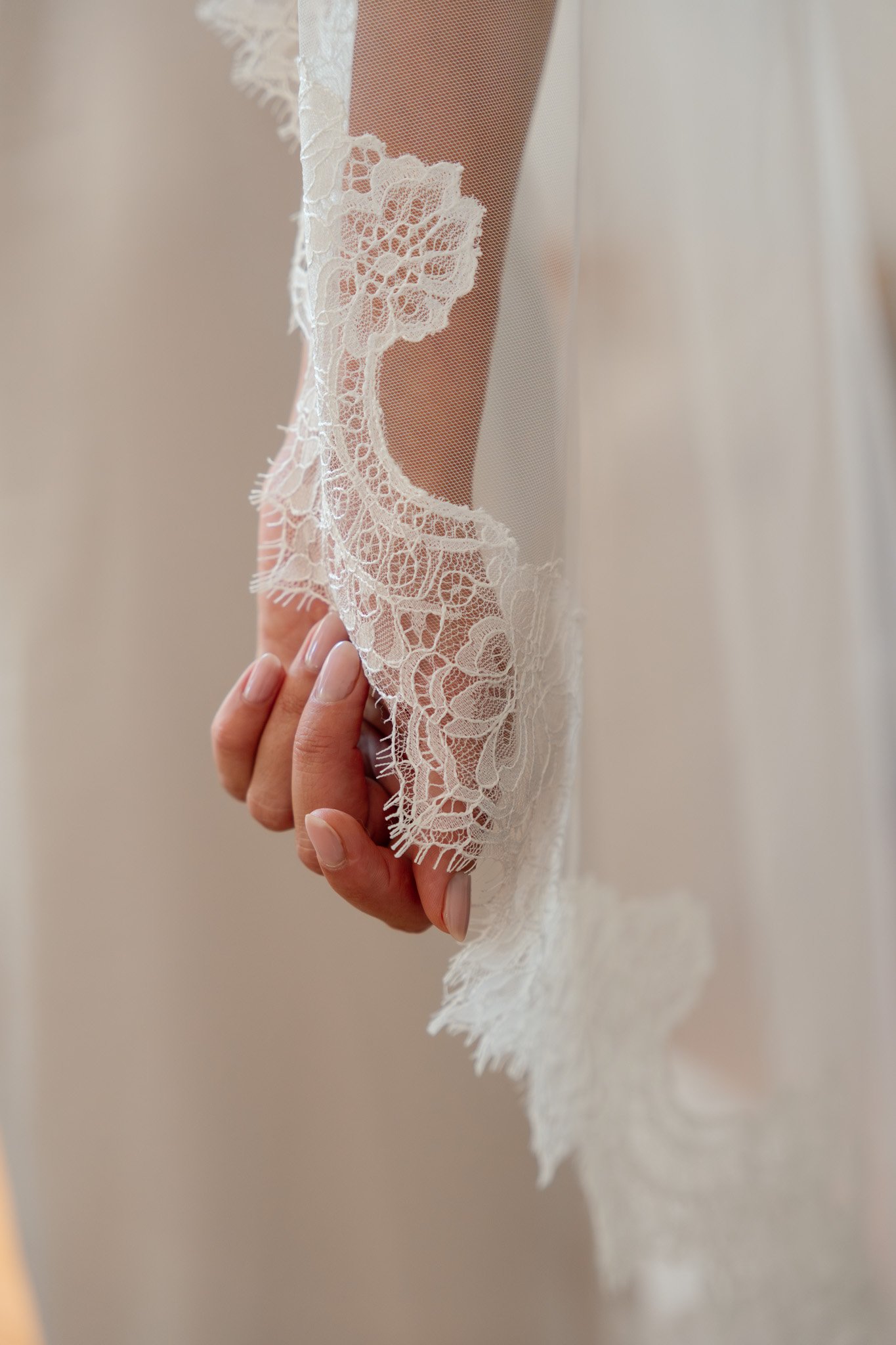 Close-up of a person holding a delicate lace fabric with floral patterns, wearing a sheer sleeve.