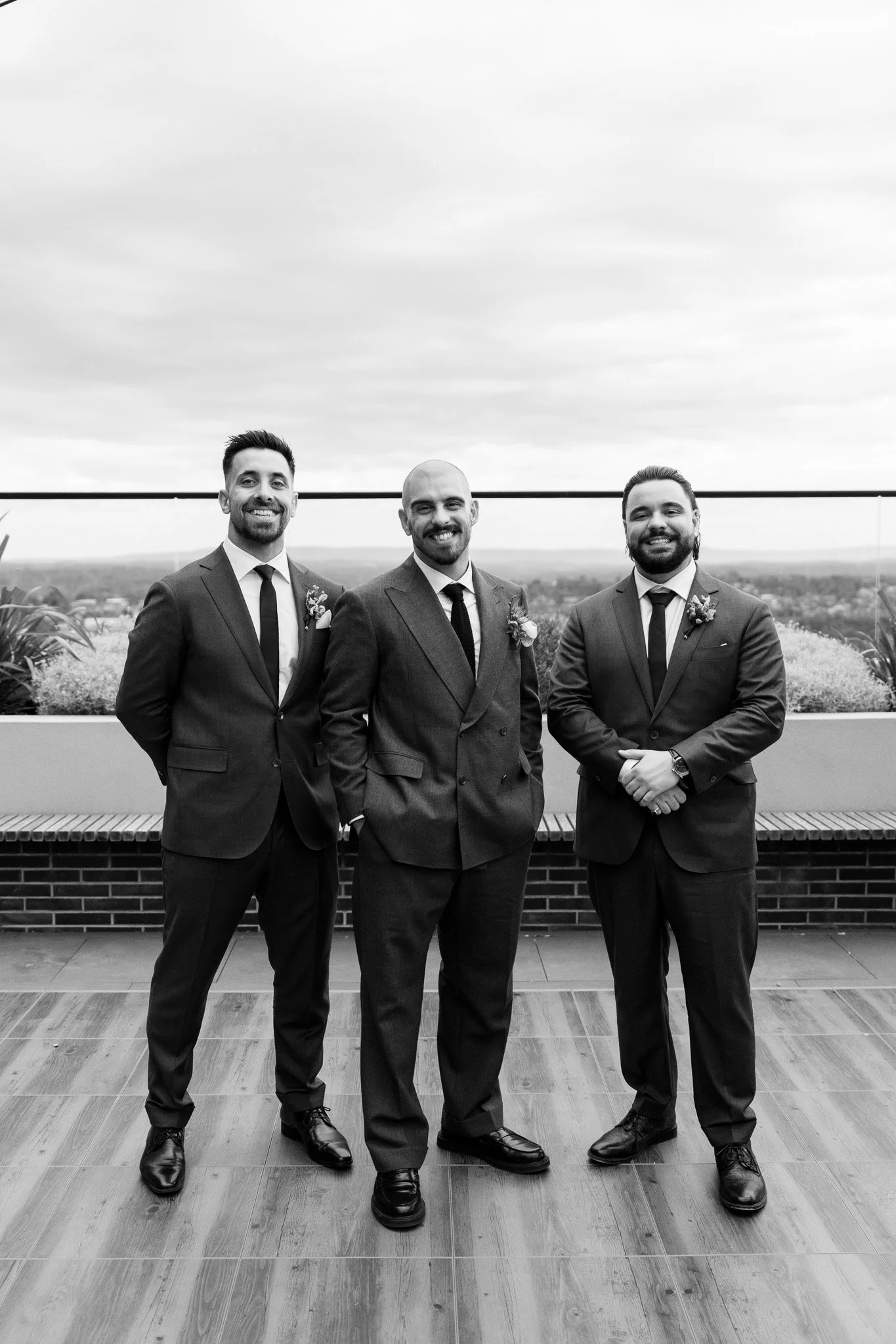 Three men in suits standing together outdoors on a rooftop with a landscape in the background, smiling for the photo.