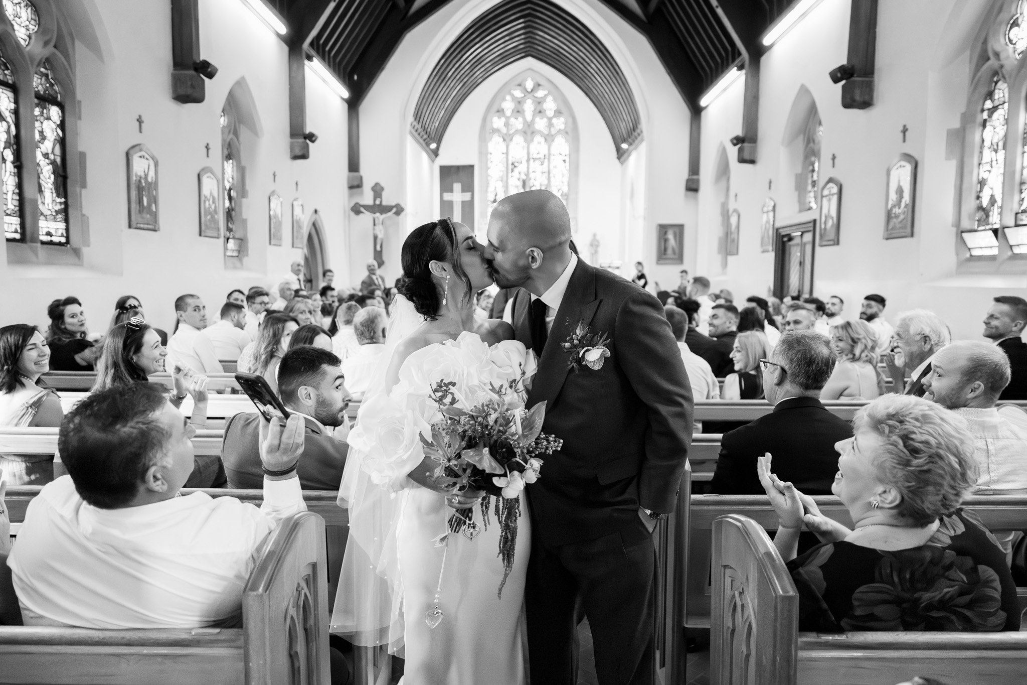 A bride and groom sharing a kiss during their wedding ceremony inside a church, surrounded by seated guests.